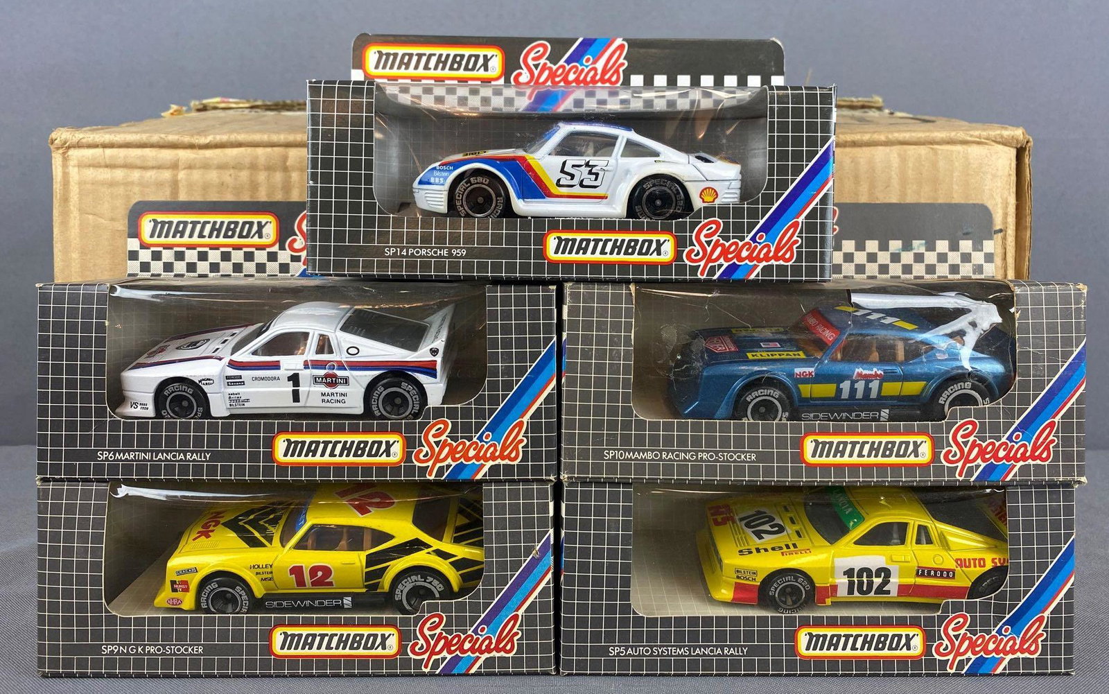 Full shipping box of Matchbox Specials die-cast: Includes (19) No. SP14 Porsche 959, (2) No. SP9 NGK Pro-Stocker, No. SP6 Martini Lancia Rally, and more. New in original packaging, some packaging shows wear