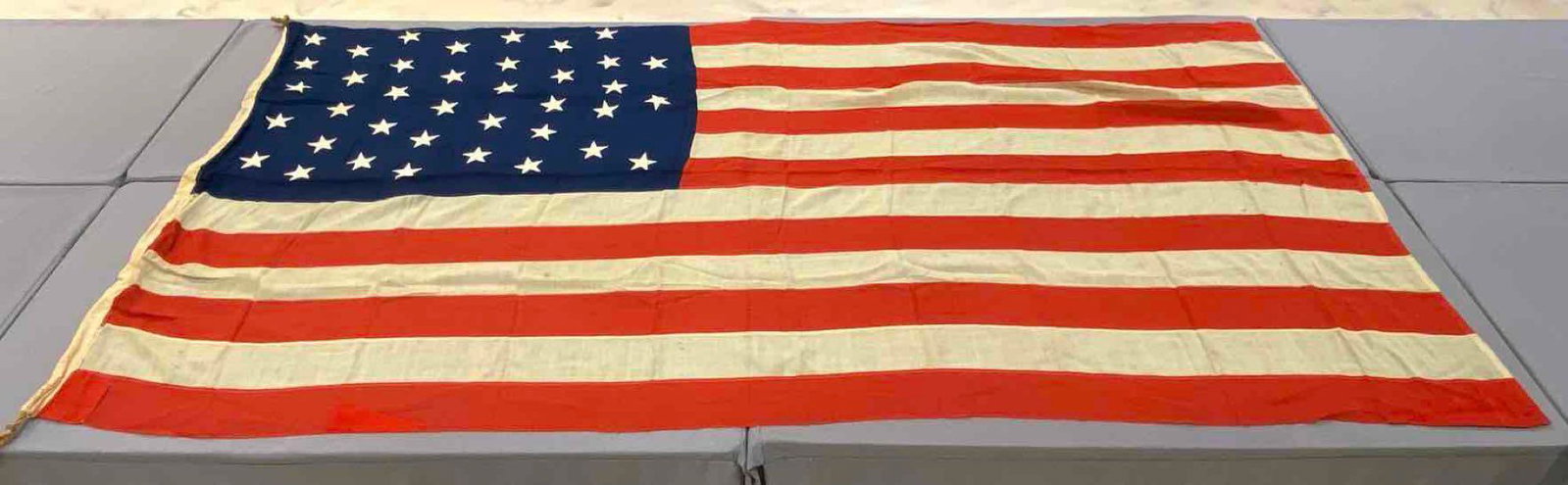 American Flag with 38 Stars: Measures 70x135 inches. Hanging rope on one end. Small holes and tears throughout.