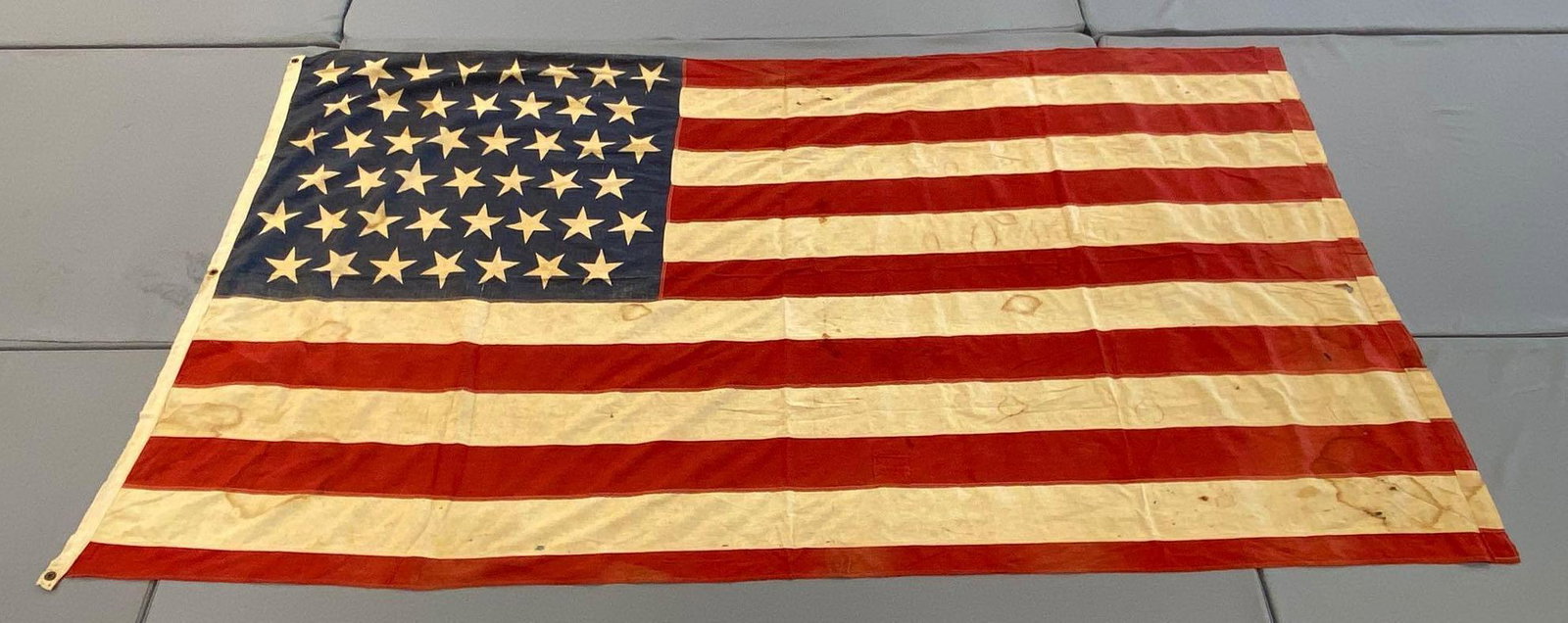 45-Star American Flag: Measures 99x56 inches. 3 grommets on hoist. Several stains, holes, and rips.