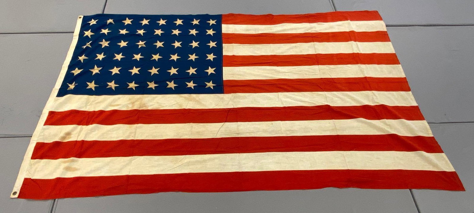 Large 48-Star American Flag: Measures 94x58 inches. Printed. 2 grommet hoist. Multiple tears through stars, some staining.