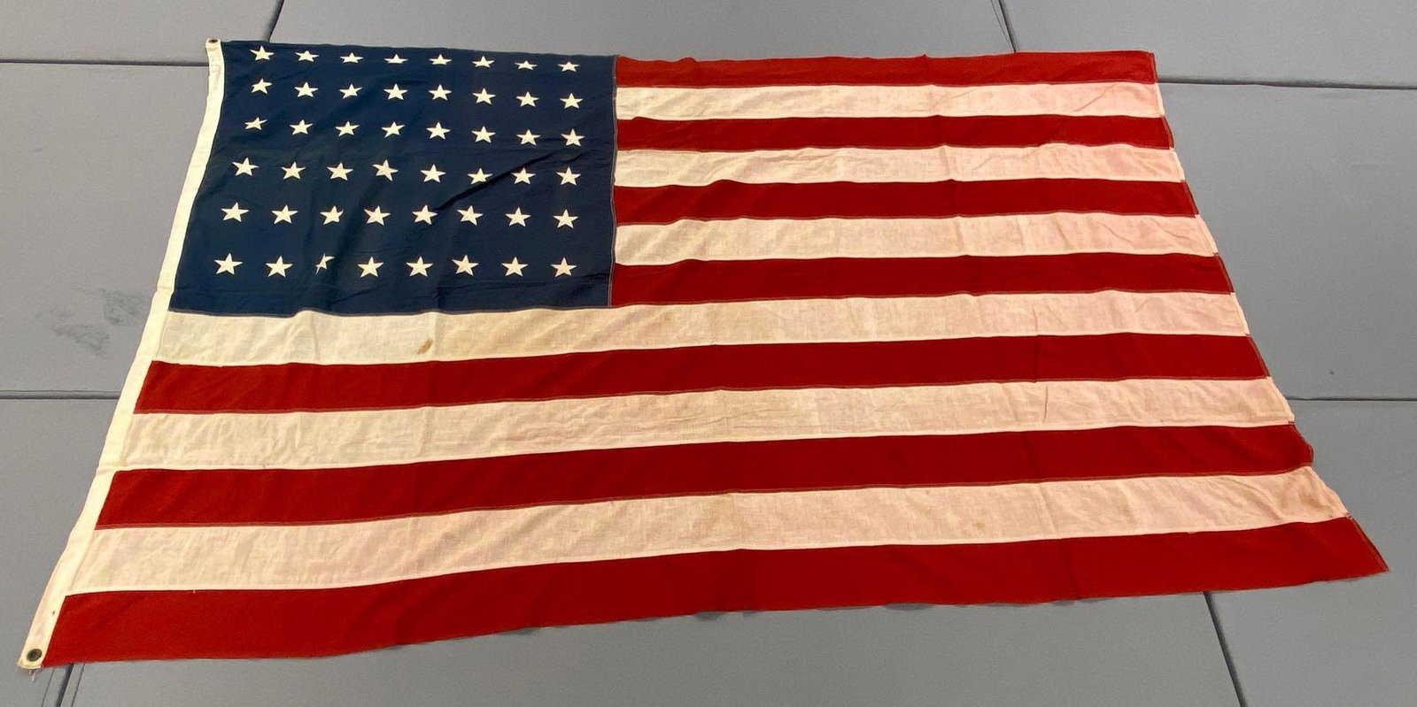 Large 48-Star American Flag: Measures 90x60 inches. 2 grommet hoist. Some staining and discoloration. White stripes are turning pink. Top left corner has the initials B.F.Z.