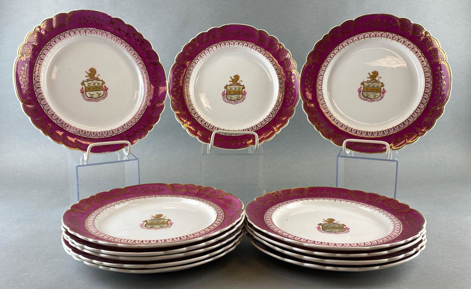 12 Piece Coat of Arms Dish Set: Deep pink and white ceramic dishes with gold tone accents. Coat of arms reads God Will Provide in Latin. Minor scratches/cracks.