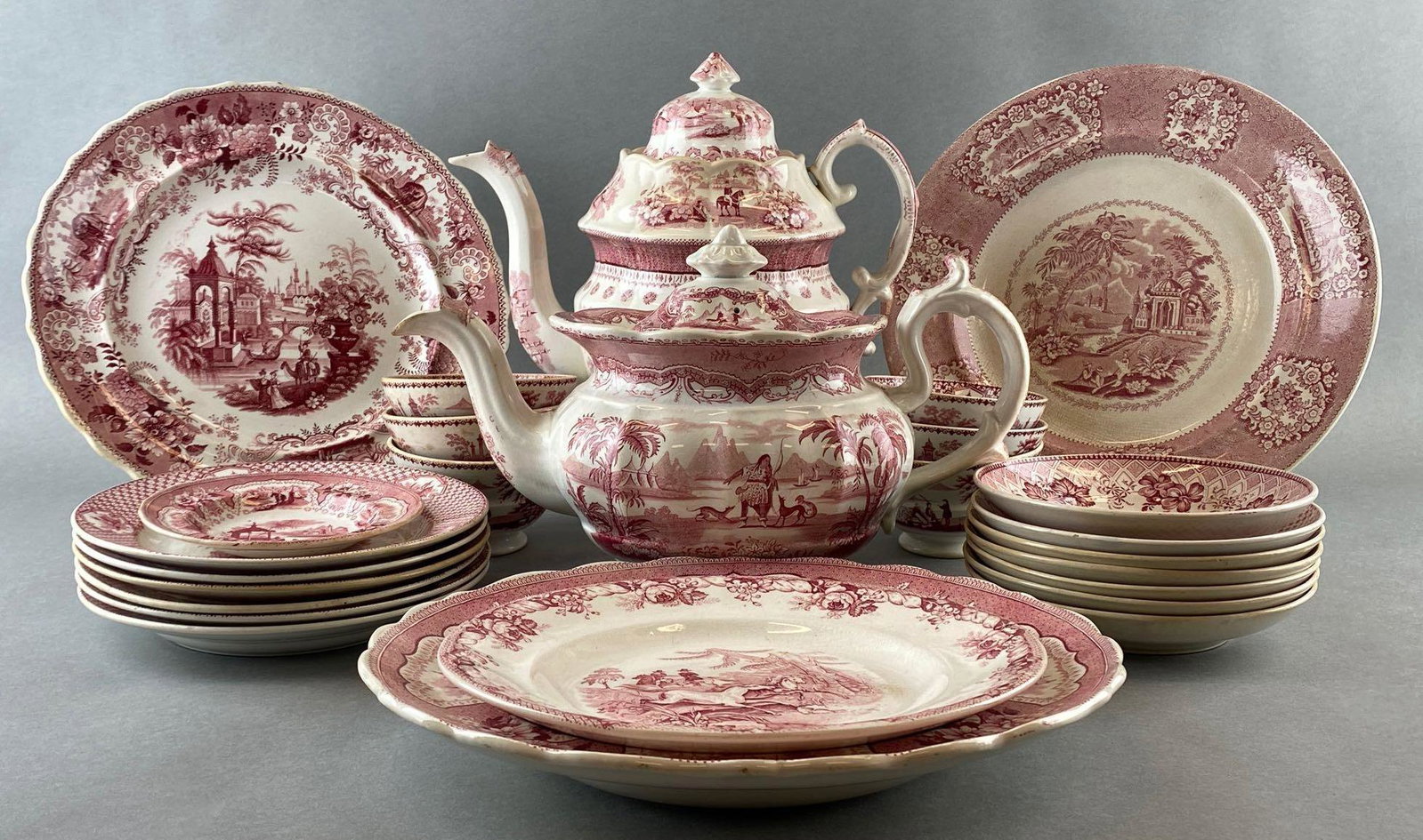 Group of 26 Red Transferware Dishes: Including teapots, plates, bowls, and more. Some chips, cracks, and crazing. Largest teapot measures 11in tall.