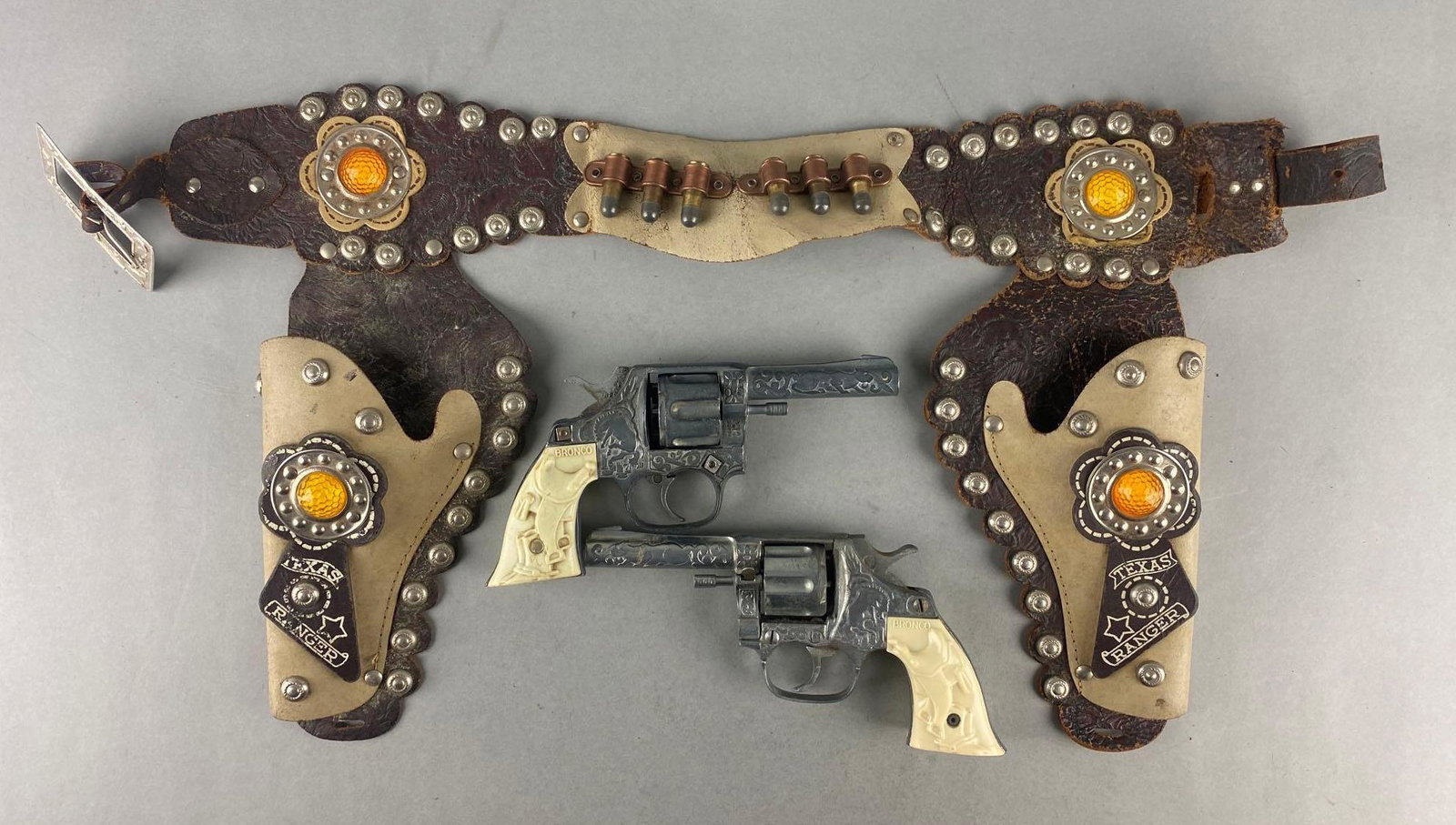 Bronco Die-Cast Cap Guns with Texas Ranger Leather Holster: 1 is in working condition, 1 is in non working condition. 1950s. Holster measures 20 inches long.
