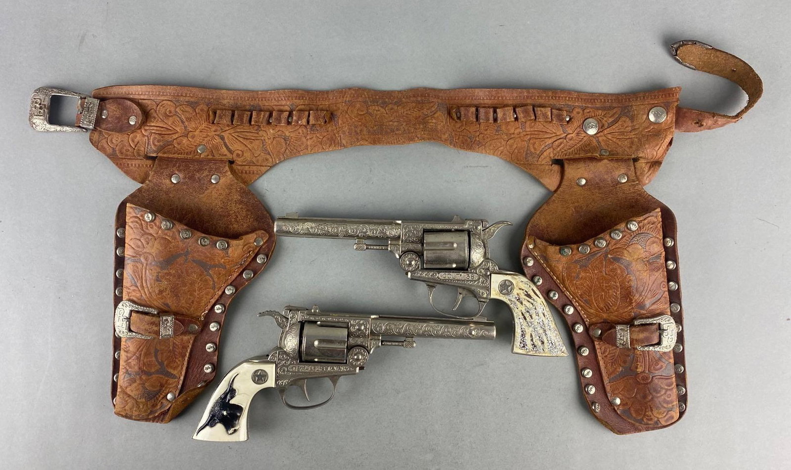 Group of 2 Die-Cast Cap Guns with Leather Holster: Includes Texan 38 and Colt 1938. Holster measures 20 inches long. 1Trigger Fires but Cylinder Does Not Rotate, 1 is in non working condition