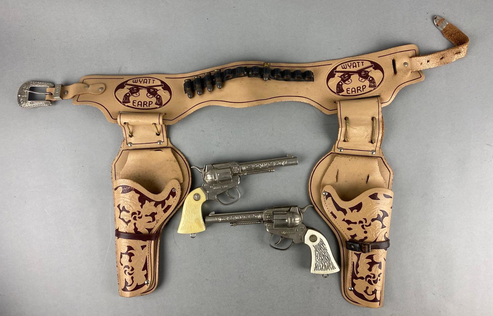 Group of 2 Die-Cast Cap Guns with Leather Holster: Includes Spitfire and Wyatt Earp. Plastic stag grips. Wyatt Earp leather holster. Holster measures 23 inches long