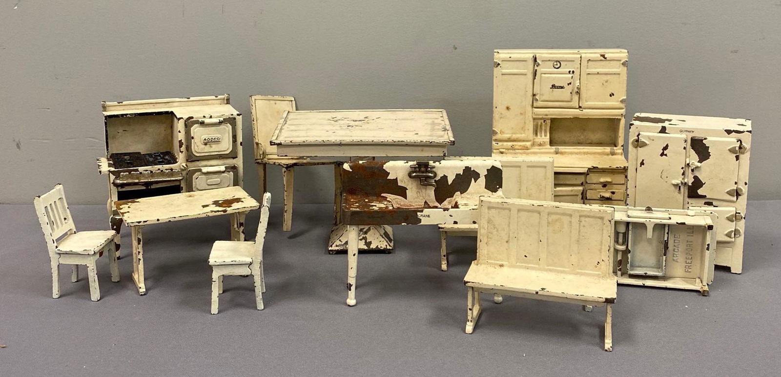 Group of 12 Doll Metal Furniture Set: Unknown set completion. Includes table, fridge, bench, and more. Missing parts, largest measures 8 x 5 1/2 x 3 inches. Paint is chipping, some pieces marked Freeport Illinois Arcade