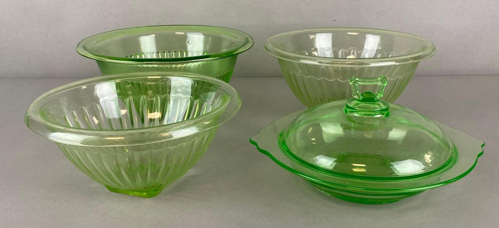 Group of 4 Green Uranium Glass Mixing Bowls and More: Includes 3 mixing bowls, and 1 covered candy dish, Some flaws and fleabites throughout, Largest bowl measures 4 3/4 x 10 3/4 x 10 3/4 inches.