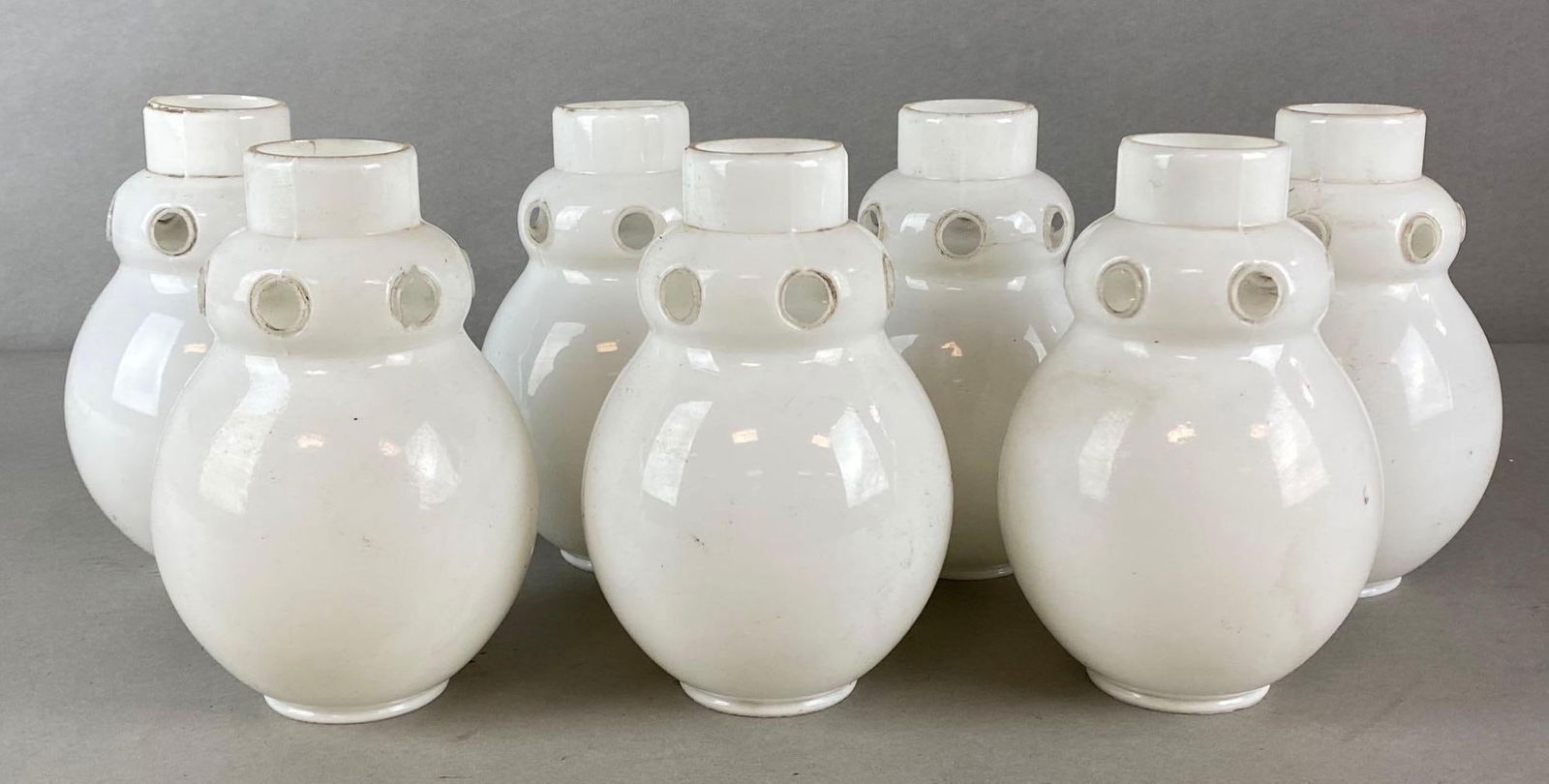 Group of 7 Vintage Art Deco Milk Glass Lamp Shades: Unique design, Some chips and cracks along holes, Fleabites, All measure 7 x 4 1/4 x 4 1/4 inches, Fitters measure 2 1/4 inches diameter.