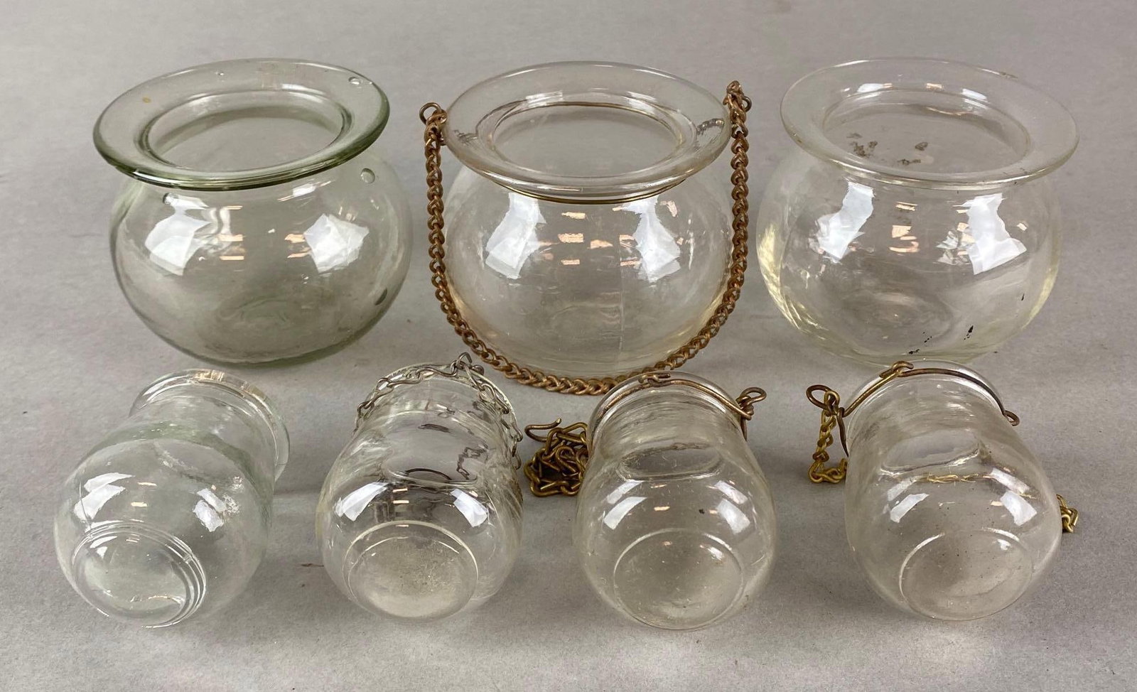 Group of 7 Clear Glass Hanging Oil Lamp Matchstick Holders: Includes (3) Large, and (4) Small, Some with chains, Some small chips along rims, Largest measures 2 1/2 x 2 3/4 x 2 3/4 inches.