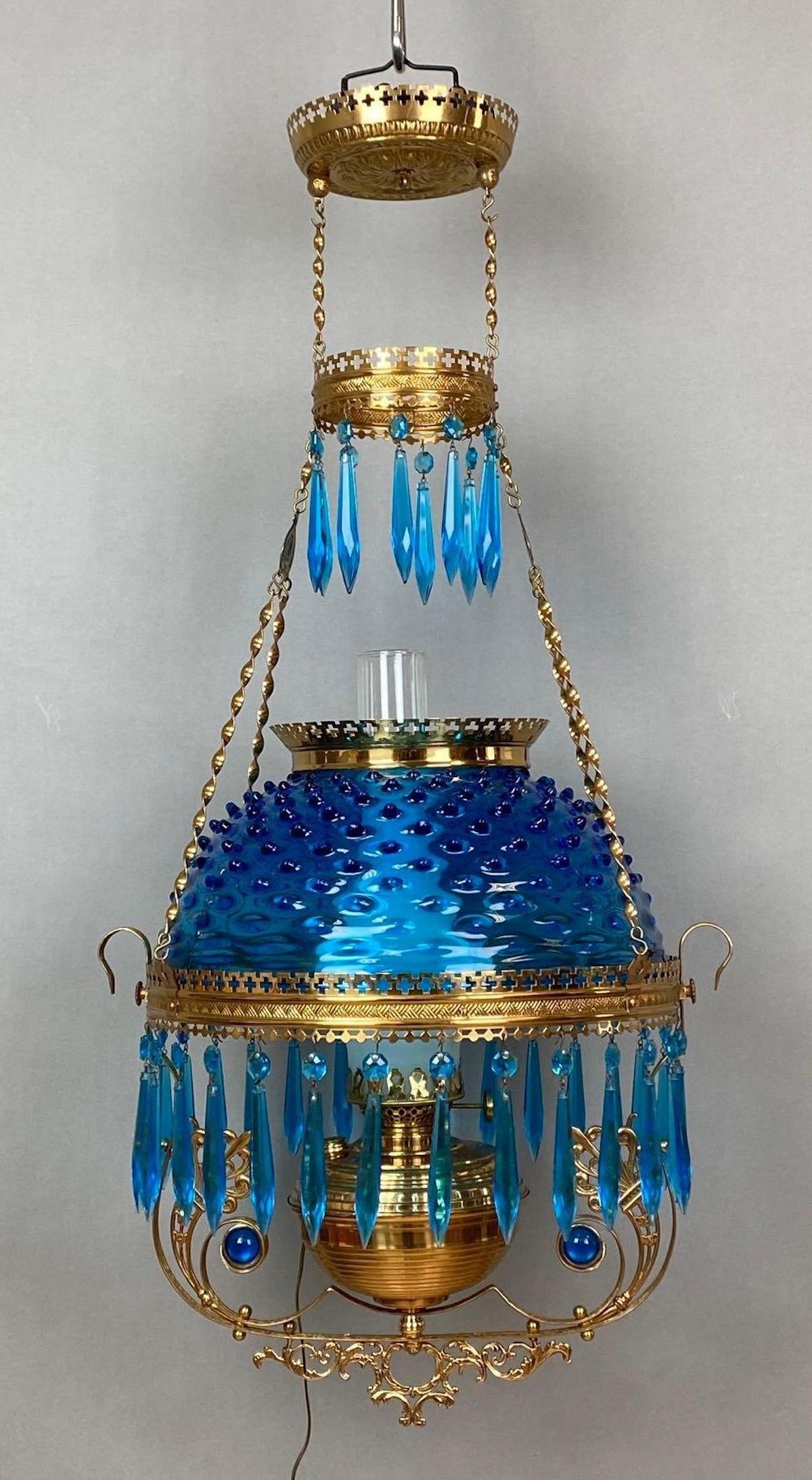 Victorian Electrified Brass Hanging Lamp with Cobalt Blue Hobnail Shade: Untested, With jeweled harp, Blue prisms, Some fleabites along rims, Shade fitter measures 13 3/4 inches across, Measures 37 1/2 x 17 x 14 1/2 inches.