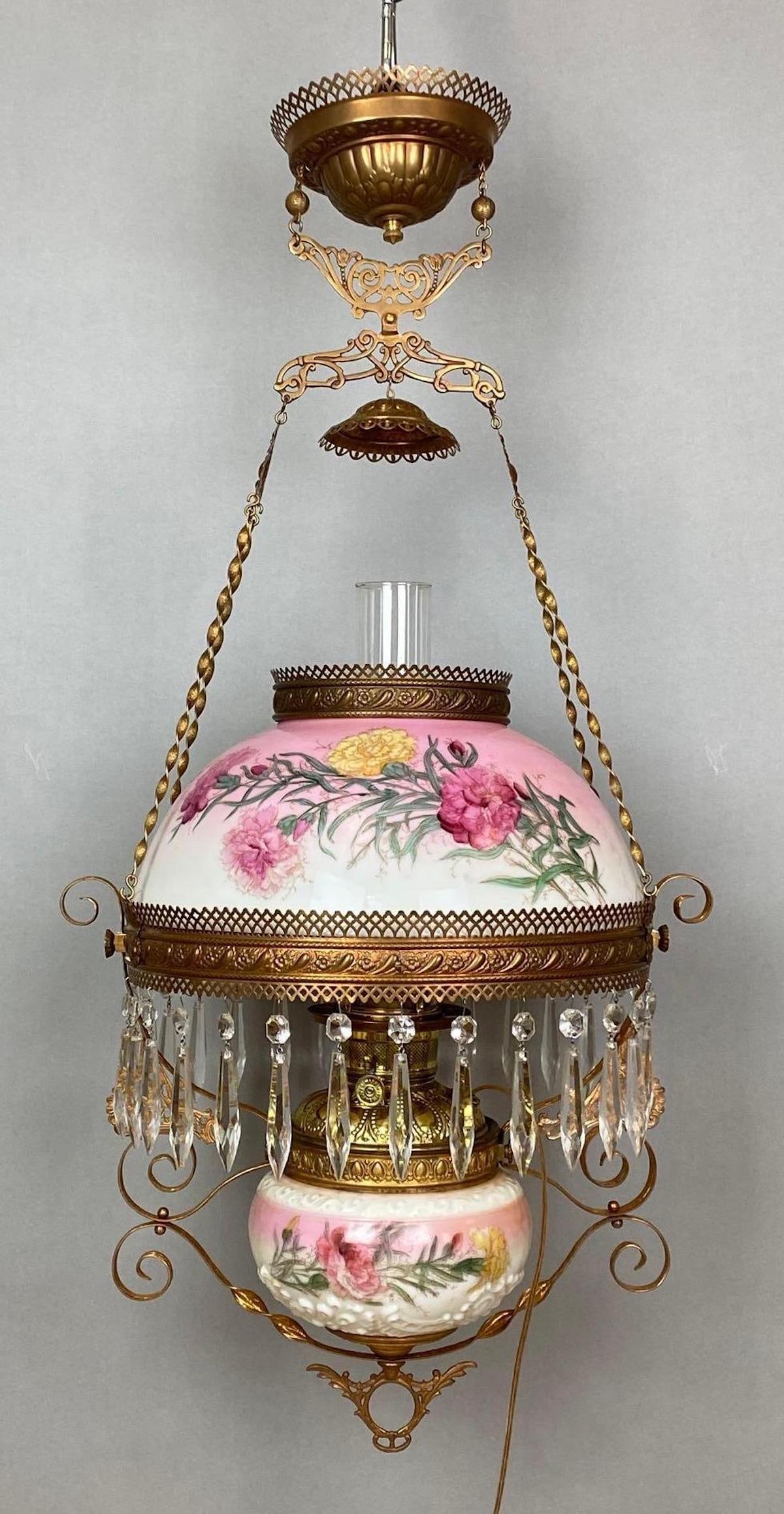Victorian Electrified Brass Hanging Lamp with Painted Milk Glass Shade: Untested, Pink painted floral milk glass shade and fount, Clear prisms, Some fleabites, Shade fitter measures 14 inches across, Measures 36 x 18 x 14 1/2 inches.