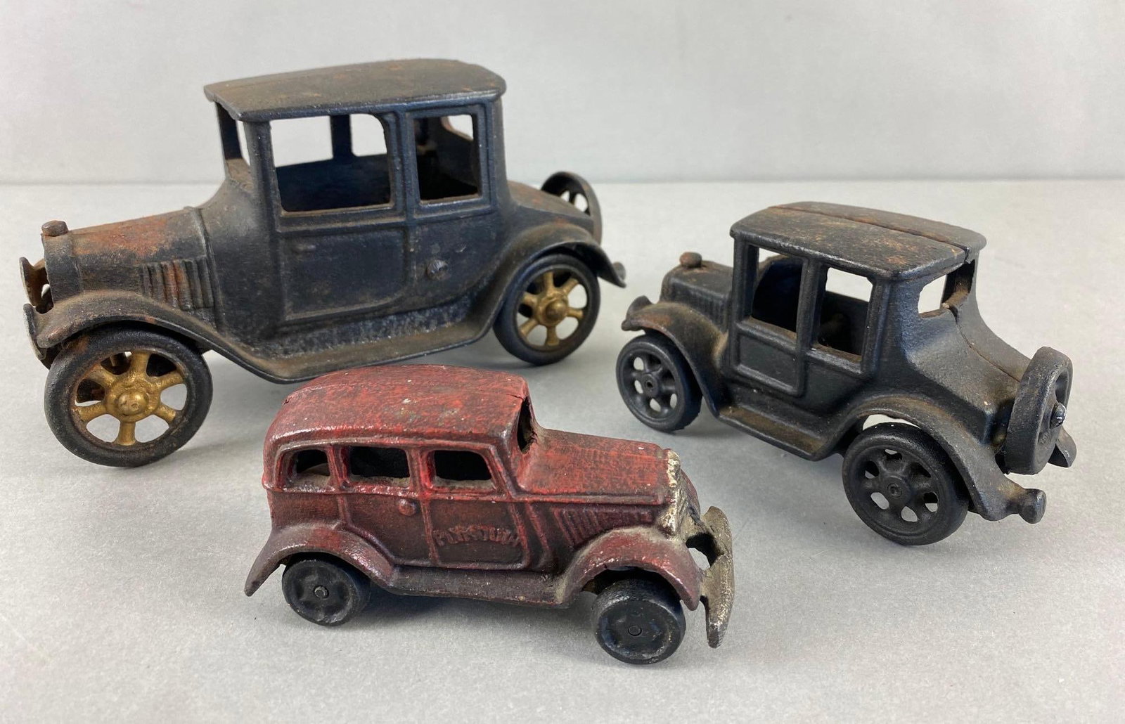Group of 3 Cast Iron Toy Cars: Includes 2 Model Ts and a Red Plymouth Sedan. All with some rust. Largest measures 4 1/4 x 8 x 3 1/2 inches.