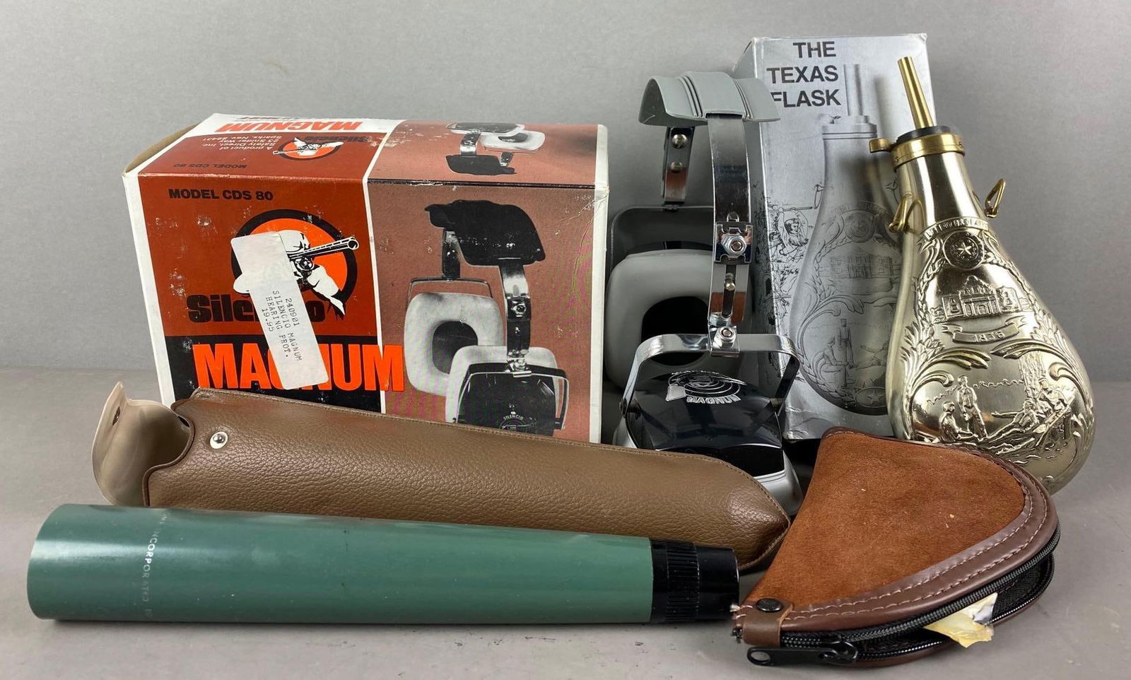 Group of 4 Assorted Gun Accessories and More: Includes Silencio Magnum Shooters Earmuffs, The Texas Powder Flask, and more. Some with case/original boxes. Flask measures 11 x 3 3/4 inches