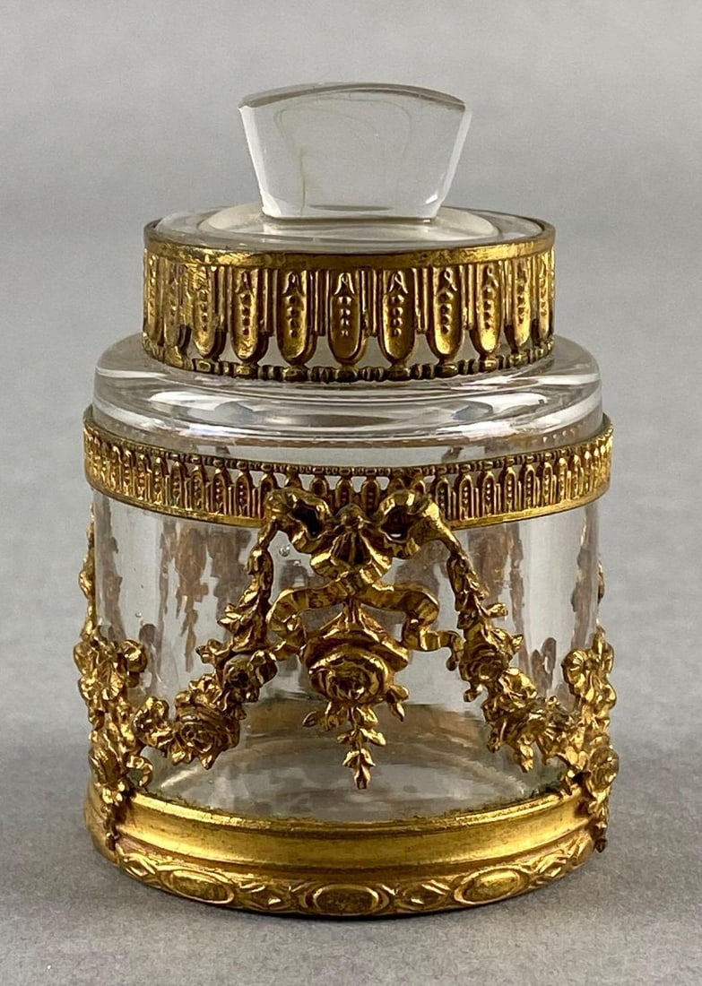 Antique French Clear Glass Perfume Bottle with Gilt Metal Casing: Floral and bow motif, Some small fleabites along rim and stopper, Measures 2 3/4 x 2 x 2 inches.