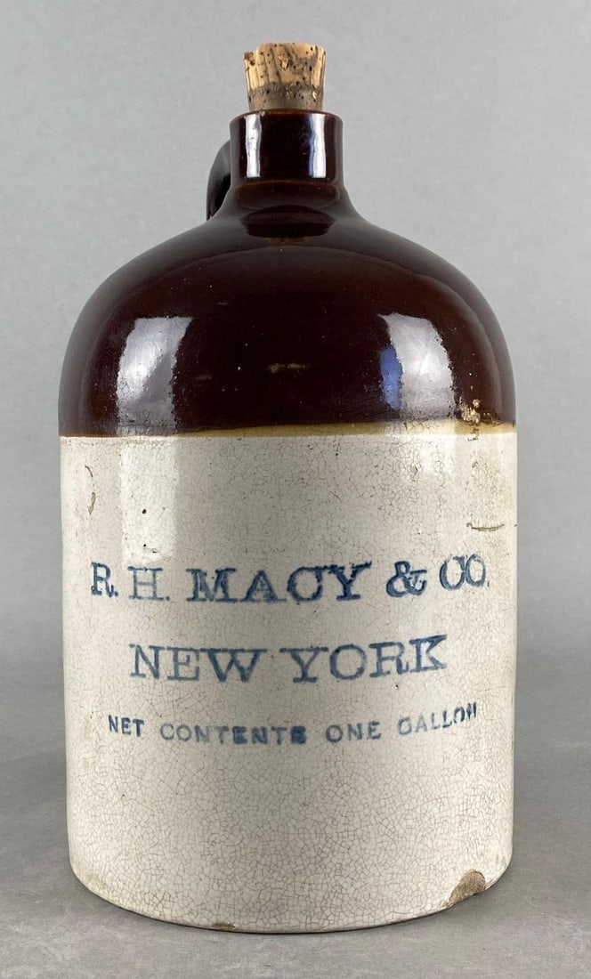 1 Gallon New York R.H. Macy and Co. Stoneware Jug: Royal Charter Pure Whiskey Paper label on opposite side, Large chip along bottom edge, Measures 11 x 6 1/2 x 6 1/2 inches.