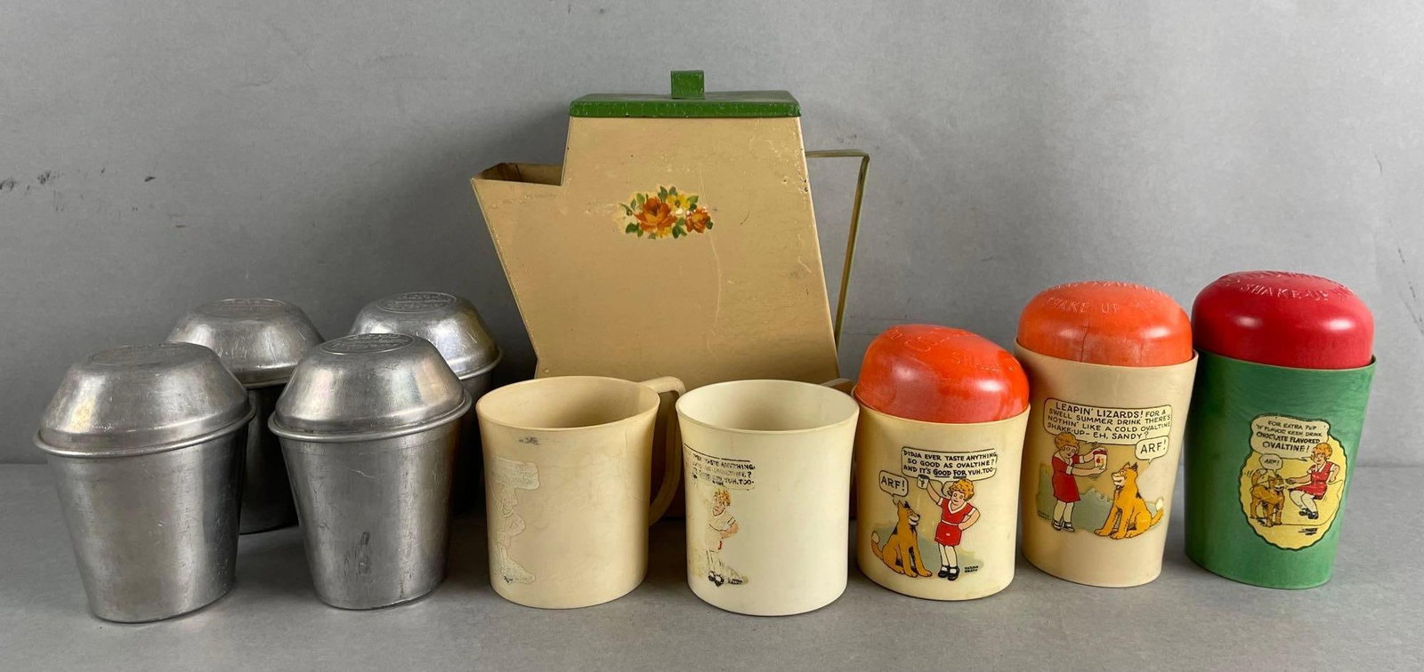 Group of 10 Little Orphan Annie Ovaltine Advertising Shake Up Cups and More: Beetleware cups and mugs, some with cracks, 4 Hemo Thompsons malted milk metal cups and lids, and pitcher that measures 8 1/4 x 7 x 3 inches