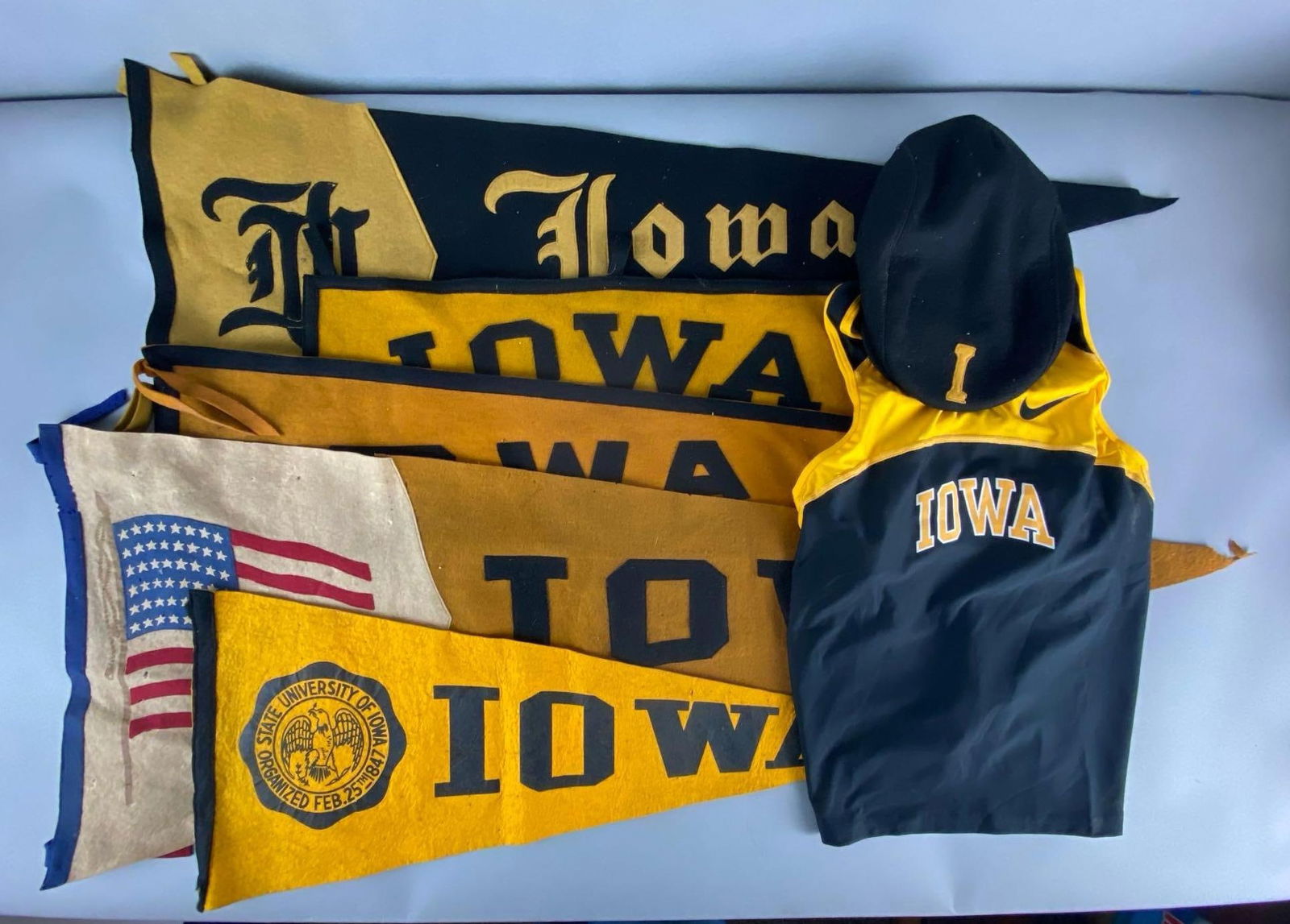 Group of 7 University of Iowa Pennants and More: Includes (5) pennants, (1) Cap, and (1) Womens Track and Field Tank size Medium, Some tears in pennants, Largest measures 16 x 43 1/2 inches.