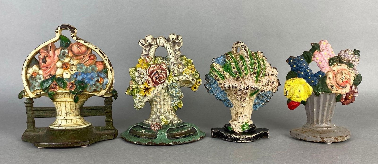 Group of 4 Cast Iron Floral Basket Doorstops: Some crazing and paint chipping throughout, Largest measures 6 3/4 x 5 3/4 x 2 1/4 inches.