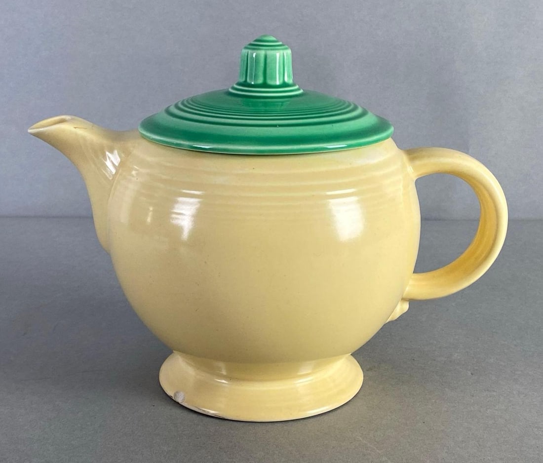 Fiestaware Buttercup Yellow Teapot with Green Lid: Small mark on top of spout, Mismatched colors, Small chip on bottom edge, Measures 6 1/2 x 8 1/2 x 5 1/4 inches.