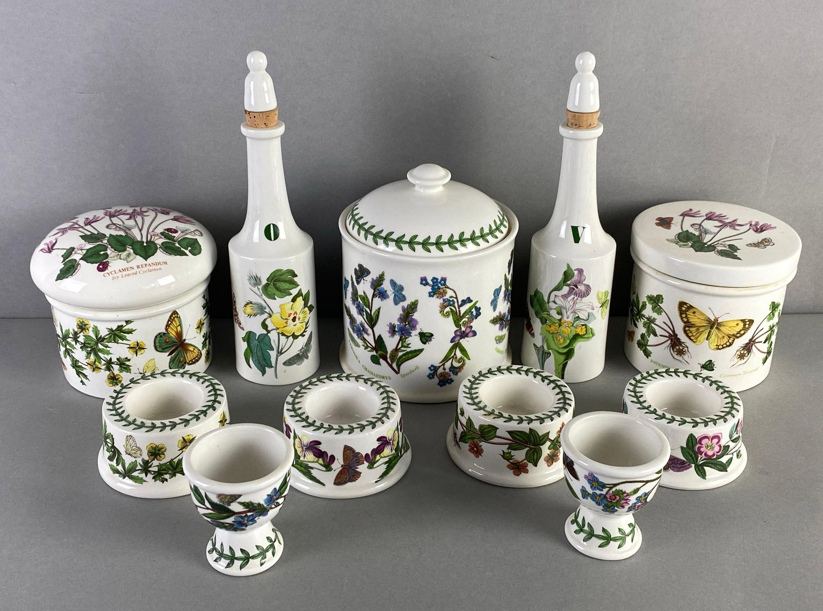 Group of 11 Portmeirion Botanic Garden Kitchenware: Made in England, 1972, includes 3 lidded containers, oil and vinegar bottles, 2 egg cups and 4 candle holders, largest measures 9 x 2 x 2 inches