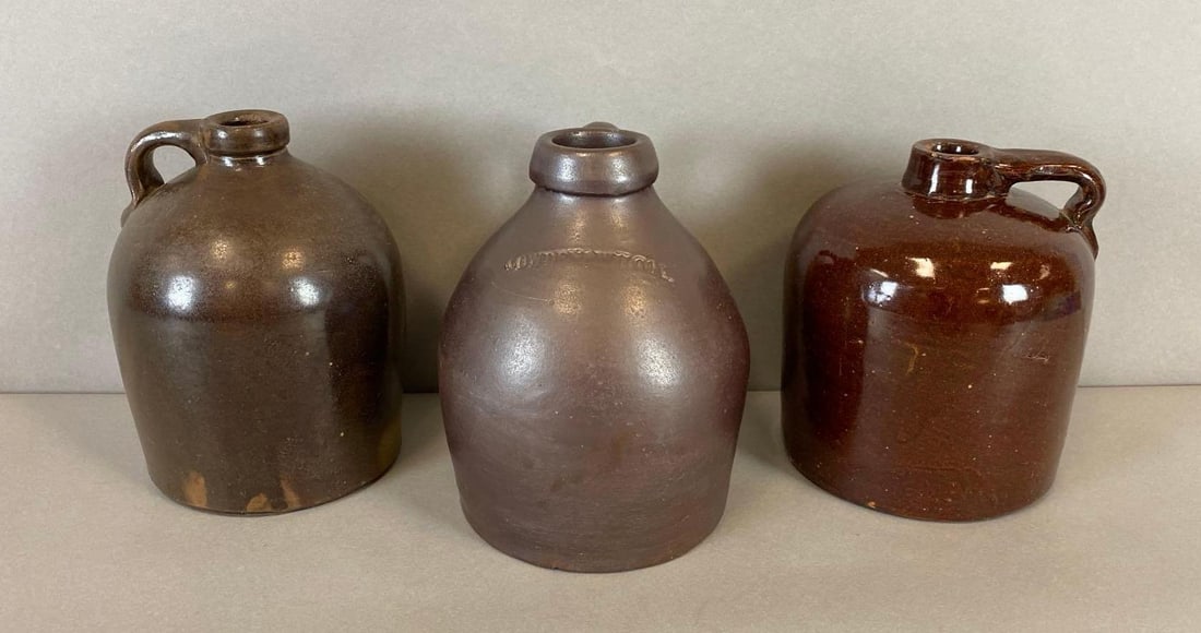 Group of 3 Antique Stoneware Jugs: Includes two more 1/2 gallon stoneware jugs. One Jug is stamped with a D. Some chips. Largest measures 7 3/4 x 5 3/4 x 5 3/4 inches.