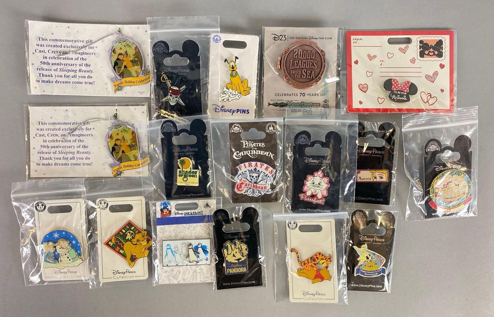 Group of 15 Disney Enamel Pins and More: Includes 2 2009 enamel Sleeping Beauty 50th Anniversary ornaments, Pirates of the Caribbean pin, Shades of Green pin and more. Largest item measures 2 1/2 x 1 3/4 inches.