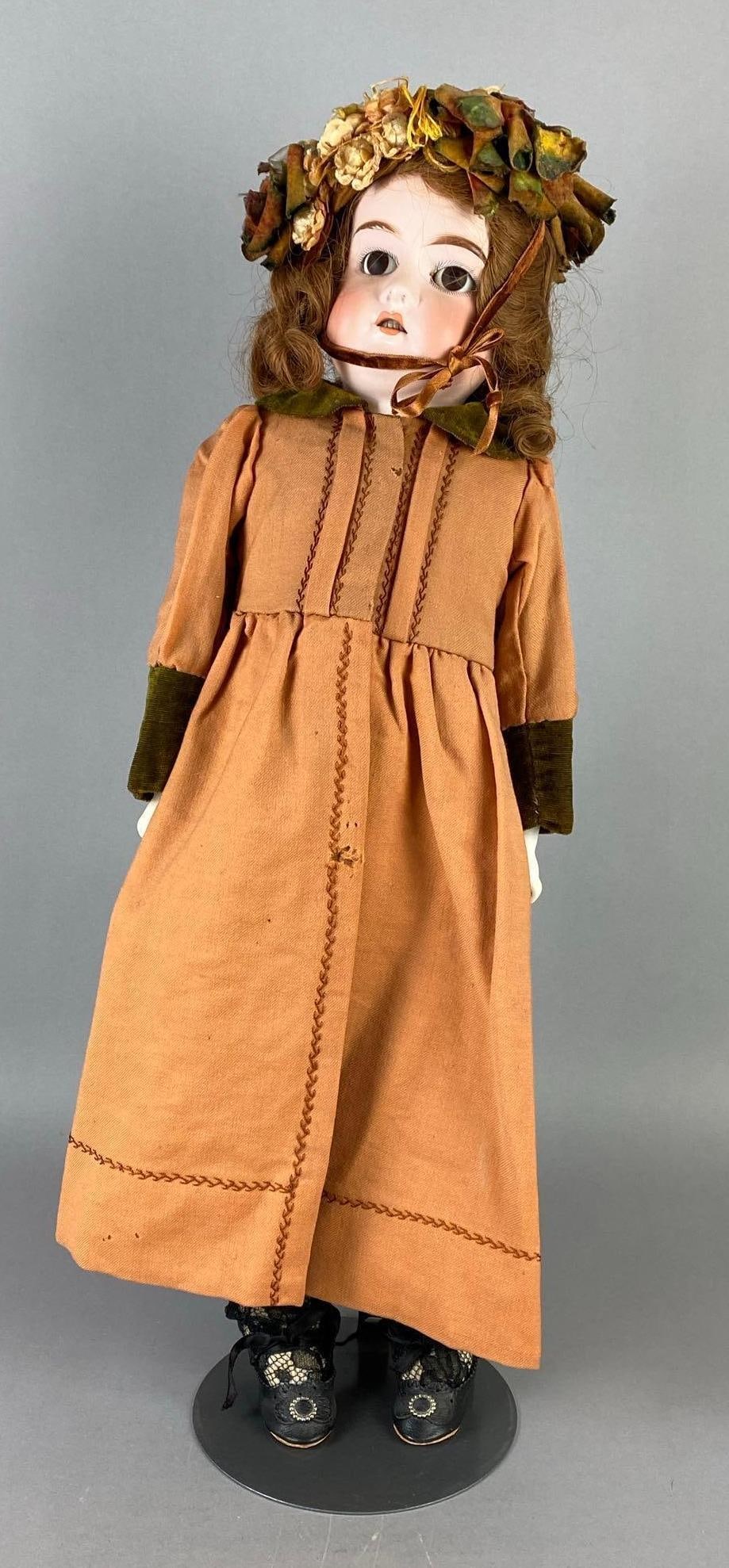 Antique German Porcelain Doll: Porcelain head and arms, Leather and cloth body and legs, Small chip and crack on right side of neck, Brown eyes, Open mouth, 6 teeth, Some holes in coat, Doll stand included, Doll measures 22 1/2 inc