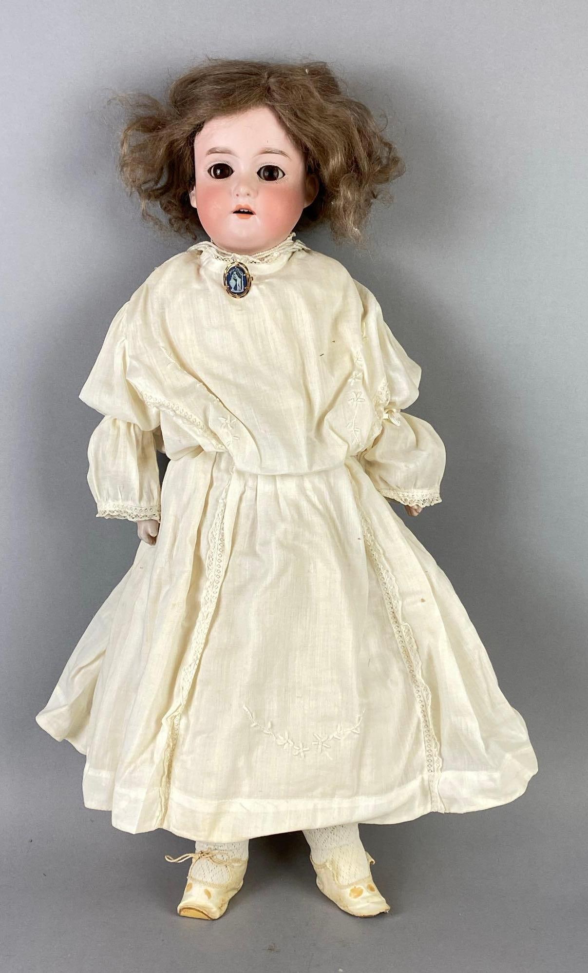 Armand Marseille German Porcelain and Leather Doll: With 10K Gold Blue Wedgewood Cameo Brooch, Porcelain head and hands, Leather body and legs. Brown sleepy eyes, Open mouth, 4 teeth, Doll measures 22 inches tall.