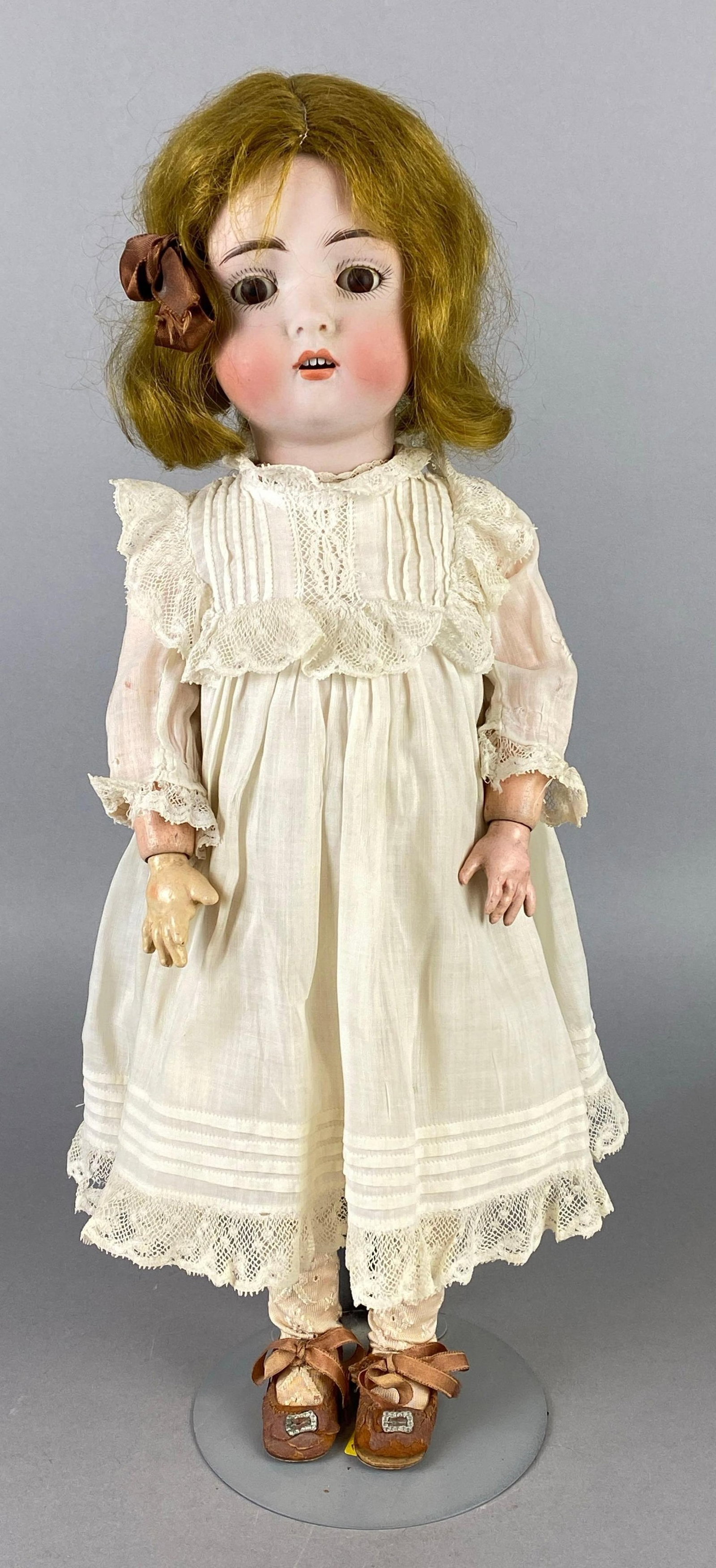 Antique German Porcelain Blonde Doll: Porcelain head with composite body and limbs, Brown sleepy eyes, Open mouth, 4 teeth, doll stand includes, Doll measures 16 1/4 inches tall.
