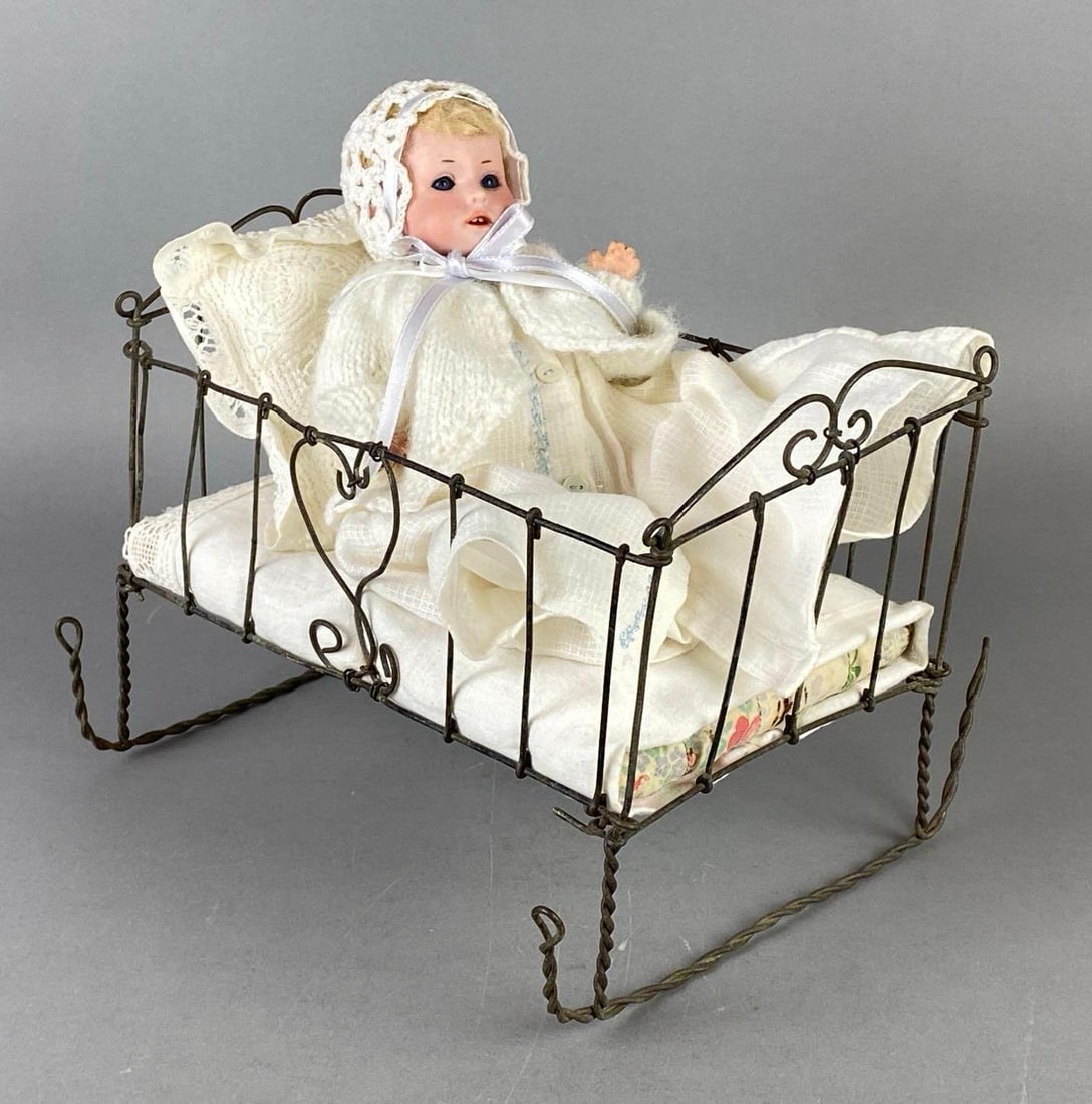 Antique DRGM Porcelain Bisque Baby Doll with Cradle: Porcelain head with composite body and limbs, Blue sleepy eyes, Bent wire cradle with linens, Cradle measures 7 1/4 x 9 1/2 x 8 1/4 inches, Doll measures 8 1/4 inches tall.