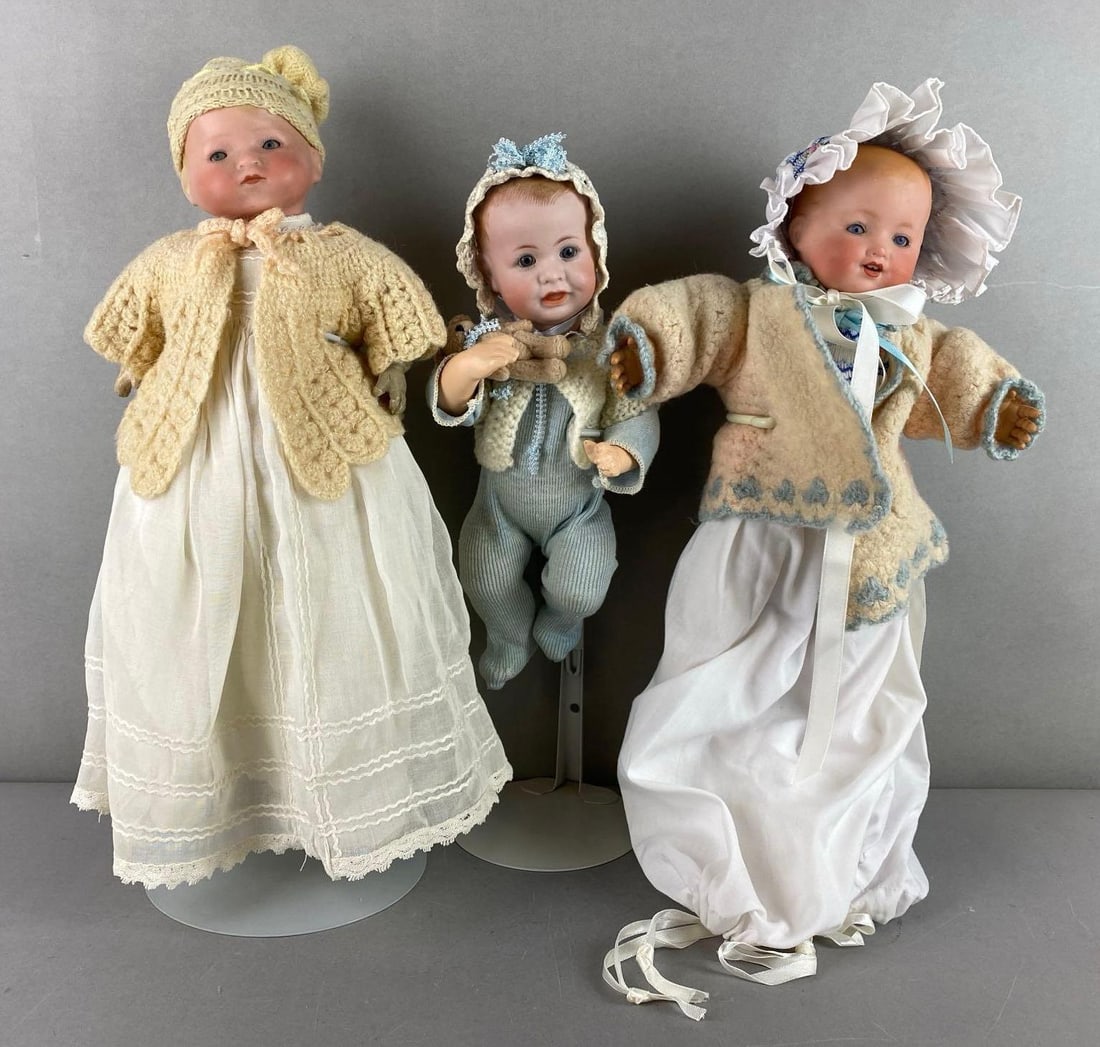 Group of 3 Porcelain Blonde Baby Dolls: 2 are Tam Germany and one is Simon and Halbig. 2 have blue sleepy eyes and one has painted blue eyes. One has crazing and chipped hands. Stands not included. Largest measures 13 inches tall.
