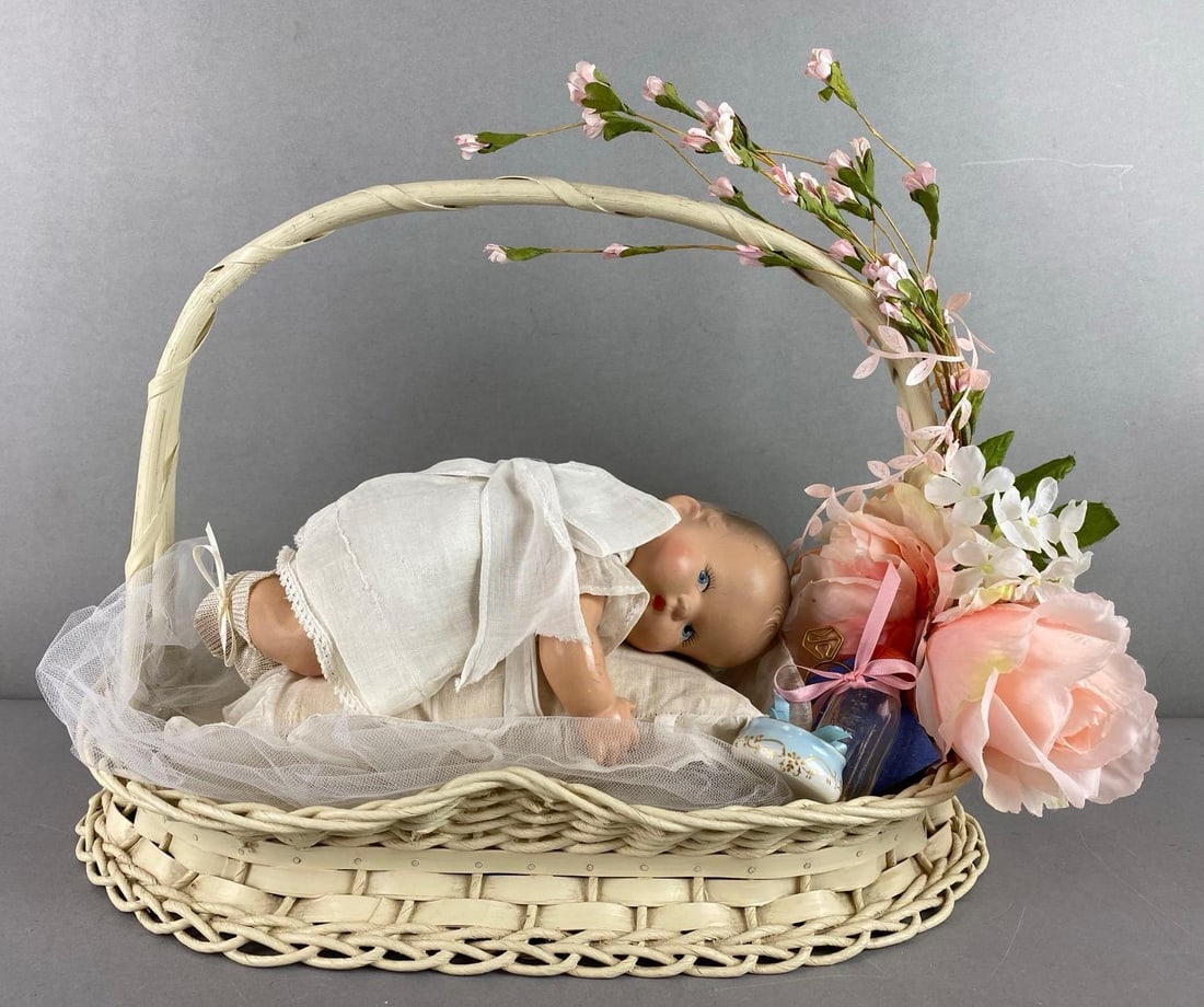 Vintage Composite Baby Doll in a Floral Basket: Wear consistent with age. Blue painted eyes. Includes glass bottle and small trinket dish. Basket measures 12 x 16 1/2 x 10 inches.