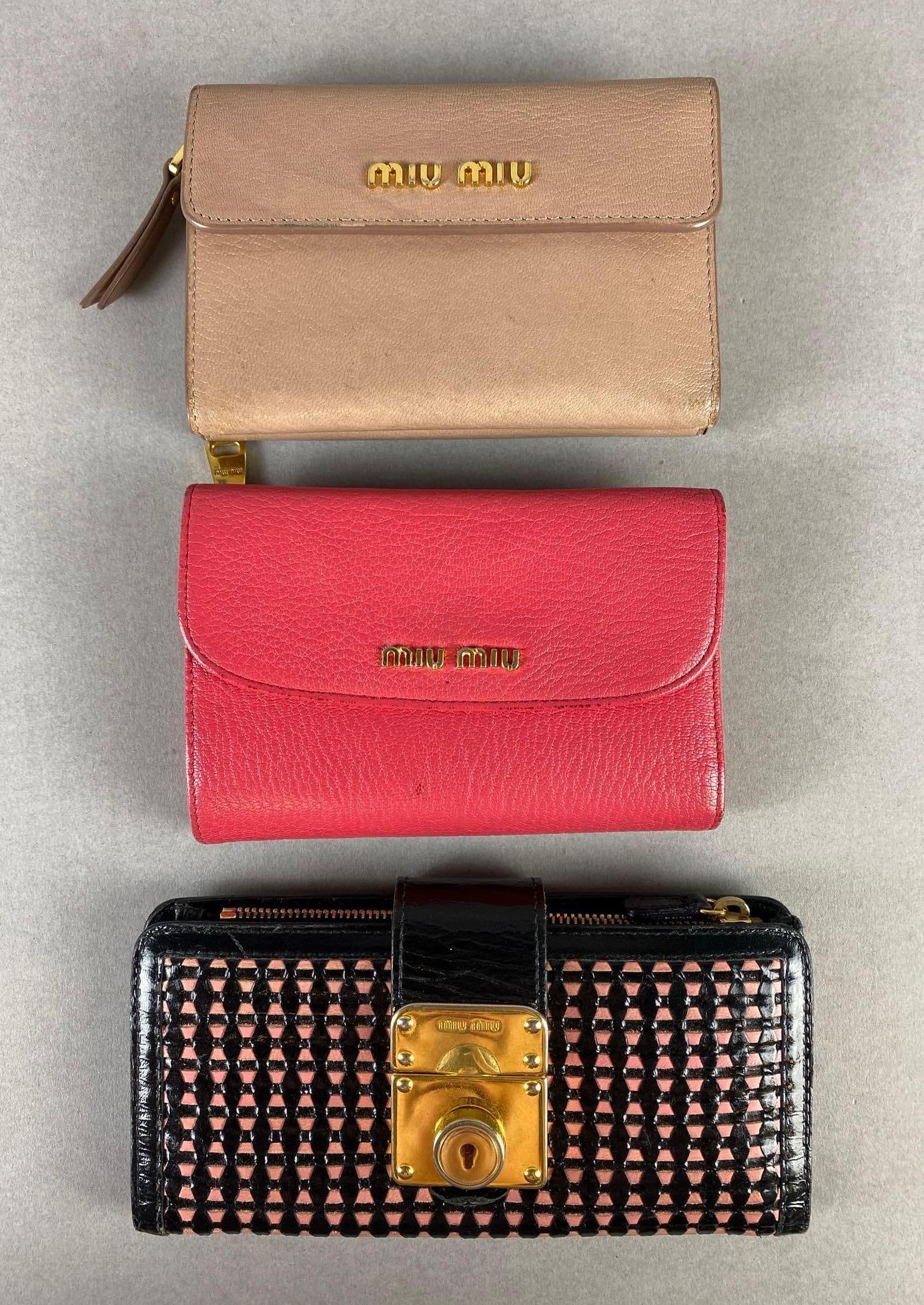 Group of 3 Miu Miu Wallets: Includes Black/Pink textured, Pink, and Beige, Some small stains on all, Largest measures 4 x 7 x 1 inches.