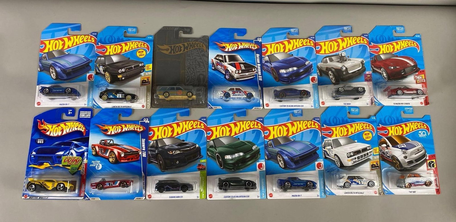 Group of 14 Hot Wheels Die-Cast Vehicles: Set of 14 various Hot Wheel die-cast vehicles that include car brands such as Triumph, Subaru, Acura, Mazda, Lancia, Nash, Suzuka, Fiat, and Datsun. All new in packaging.