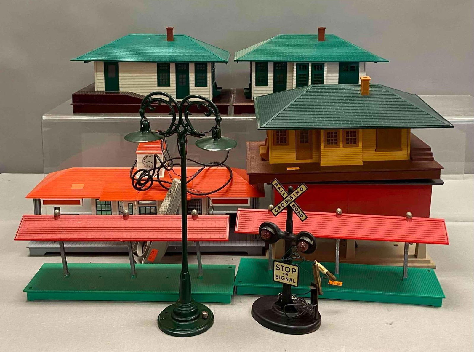 Group of Assorted Lionel Trains O Scale Model Buildings and More: Includes Street lamps, Stations, and more. Largest measures H 5 x W 6 x L 15 inches. Stand not included.