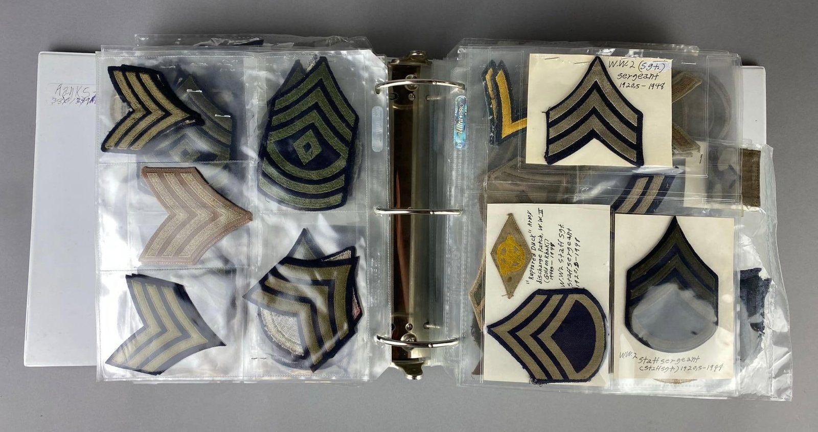 Group of 100+ US Military Insignia Patches Album: Includes WW2 US Military Staff Sergeant, Army Discharge patch, some German patches, and more. Album measures H 6 x W 12 x L 12 inches.