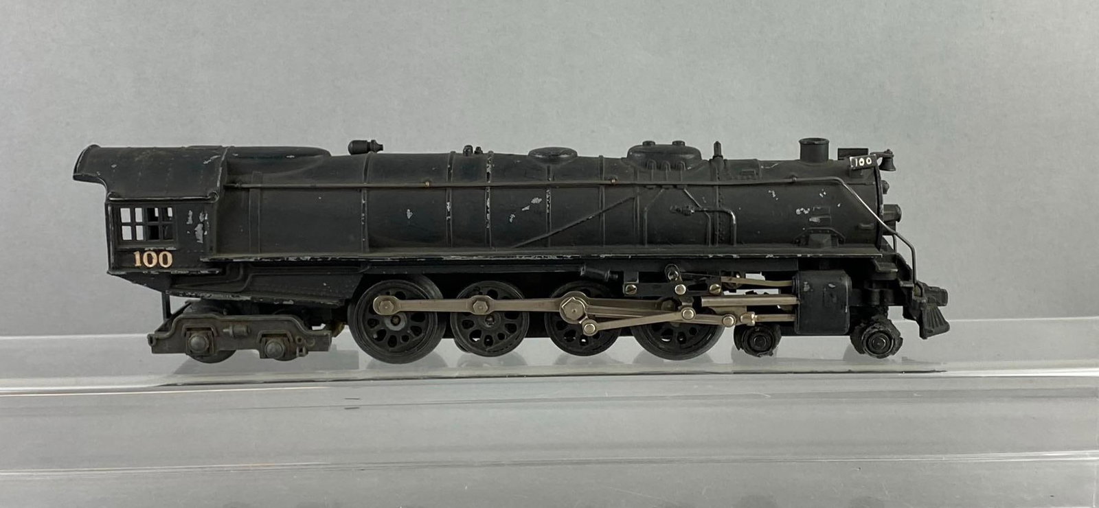 Lionel Trains O Gauge No. 100 Steam Locomotive: Untested. Front wheels are worn with age. Measures H 3 x W 2 x L 12 1/2 inches. Stand not included.
