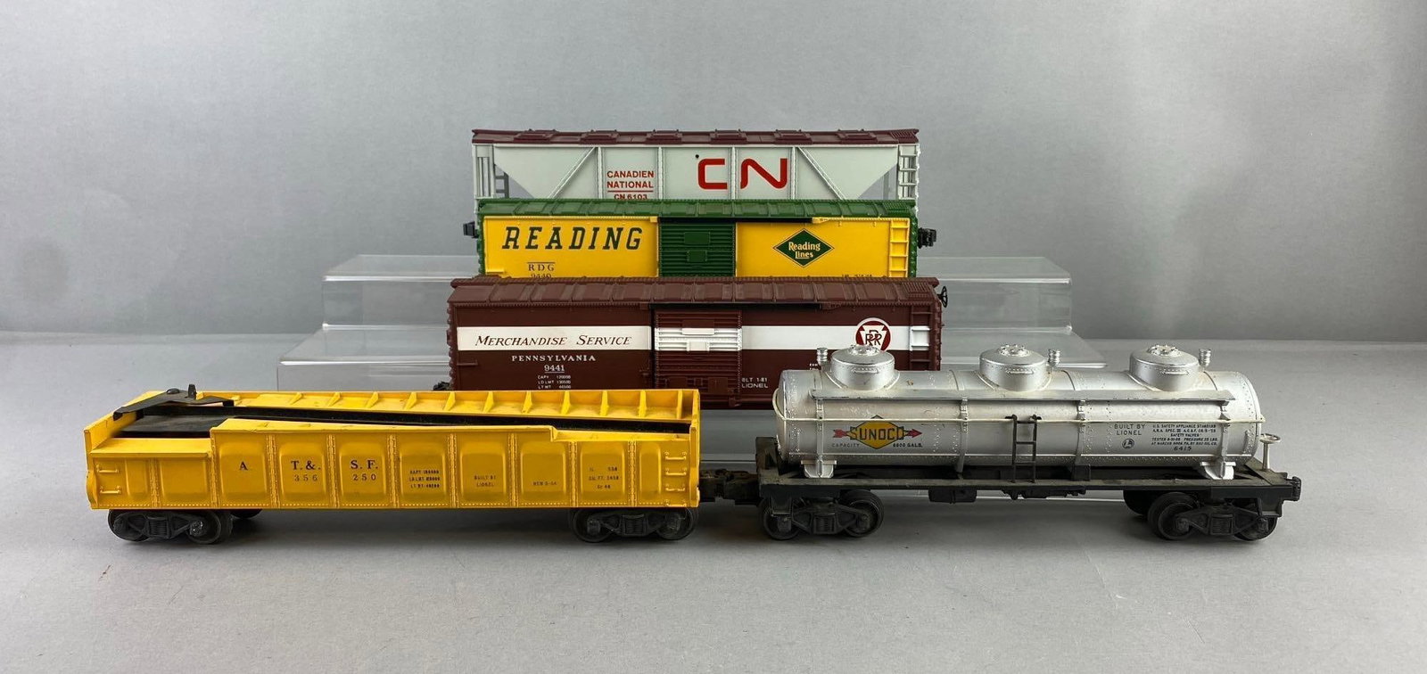 Group of 5 Lionel Trains O Gauge Boxcars and More: Includes oil tanker, gondola, and more. Largest measures H 3 x W 2 1/2 x L 12 inches. Stand not included.