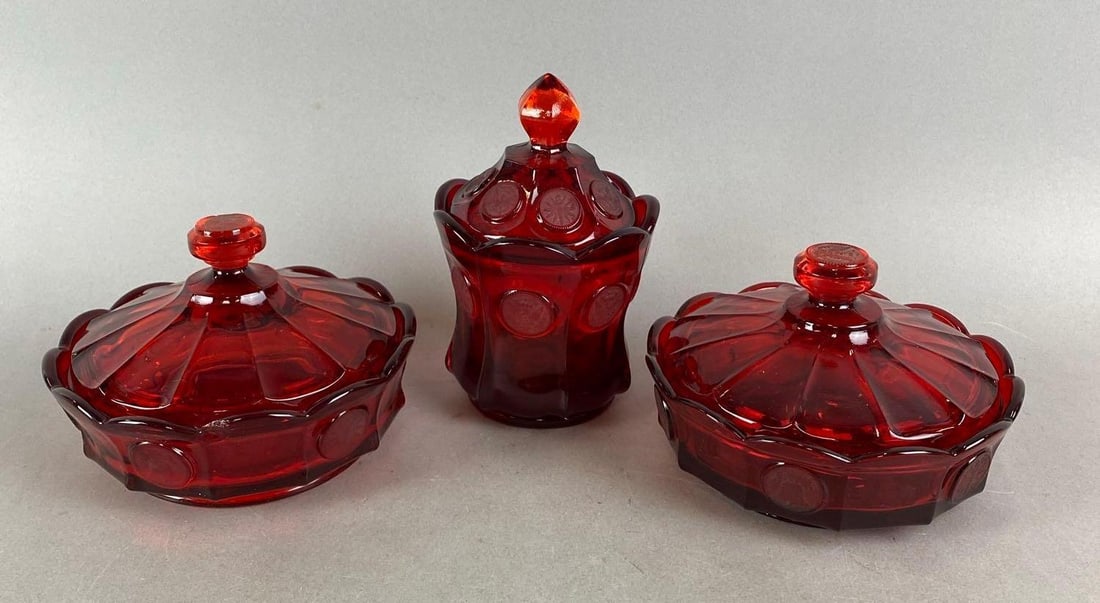 Group of 3 Fostoria Ruby Coin Items: Includes 2 Covered Candy Dishes and a covered Candy Jar. One dish has a chip and one has an original sticker. Largest Item measures H 4 x W 6 1/4x D 6 1/4 inches.