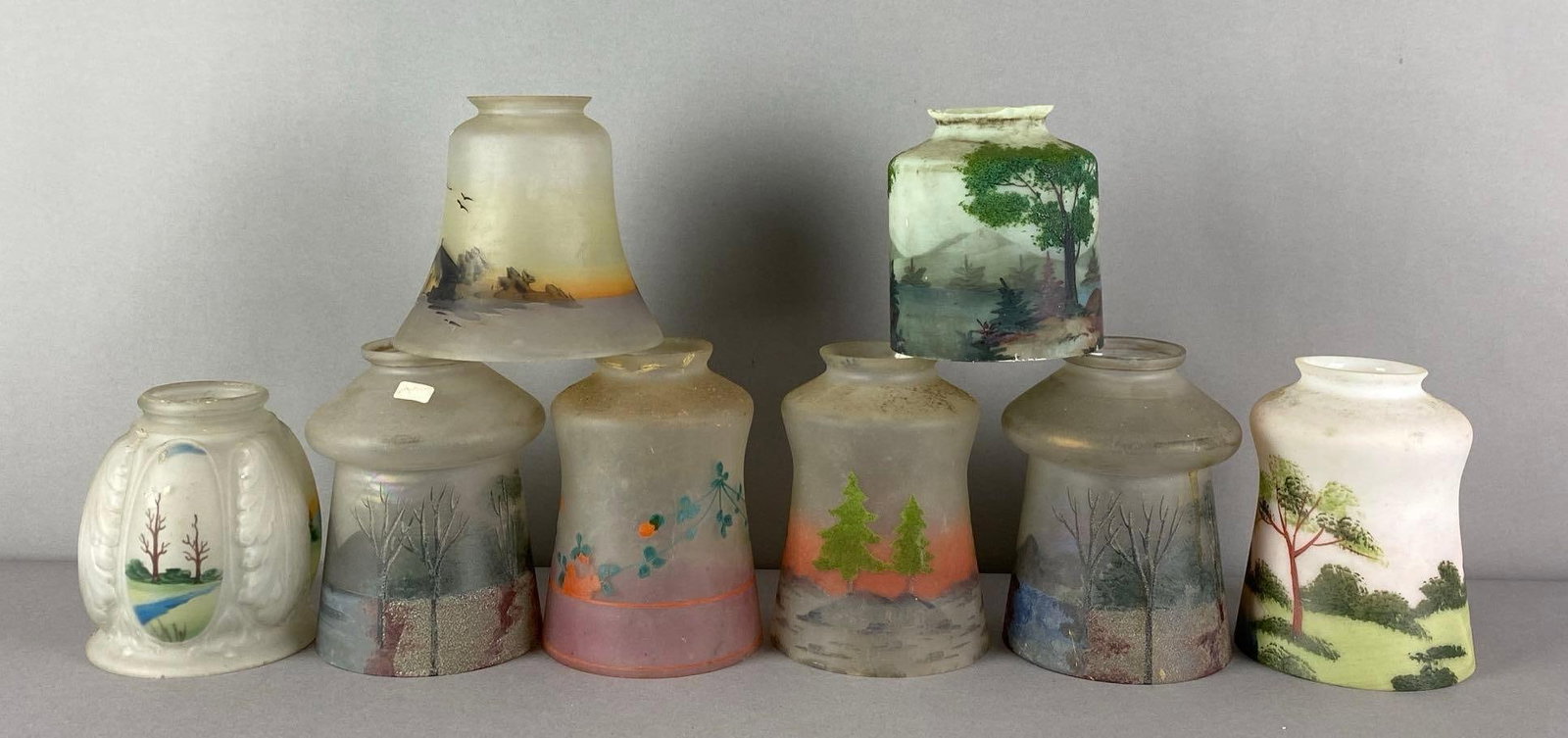 Group of 8 Hand Painted Frosted Glass Lamp Shades: Features forests, island, flowers and more, Some fitters chipped or show fleabites, largest measures 5 1/2 inches H x 4 inches W with a 2 inches fitter