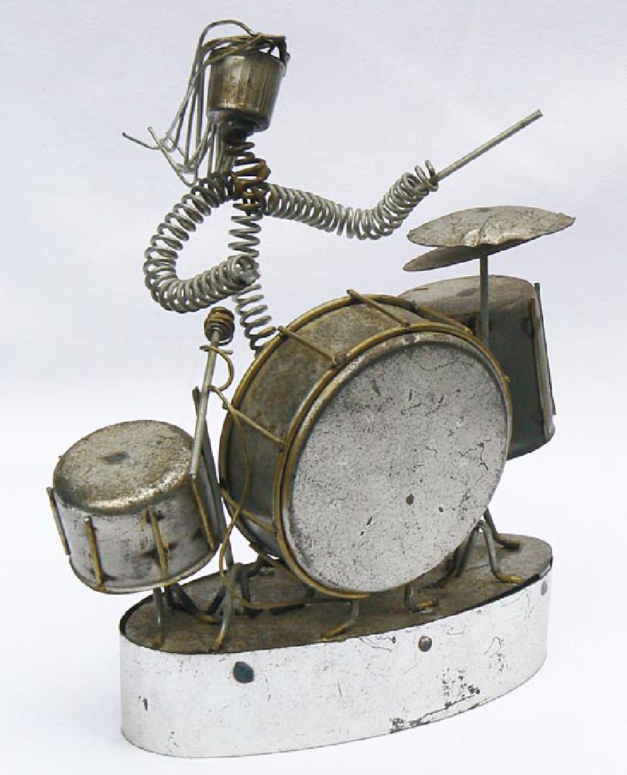 Folky metal drummer assemblage wind up music box.: This folky metal drummer assemblage is actually a wind up music box. The drummer is constructed of springs, heavy wires, and light metal. The drums and stage are also all metal. The music box mechanis