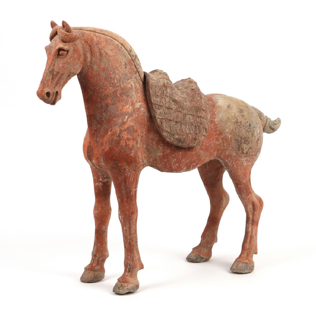 TANG DYNASTY CAPARISONED HORSE: China, c. 618-906 A.D., reddish earthenware with polychrome, the horse standing on all fours with removable saddle having combed details, subtle modeling details on neck, tail, and face, h. 15-1/4 w. 