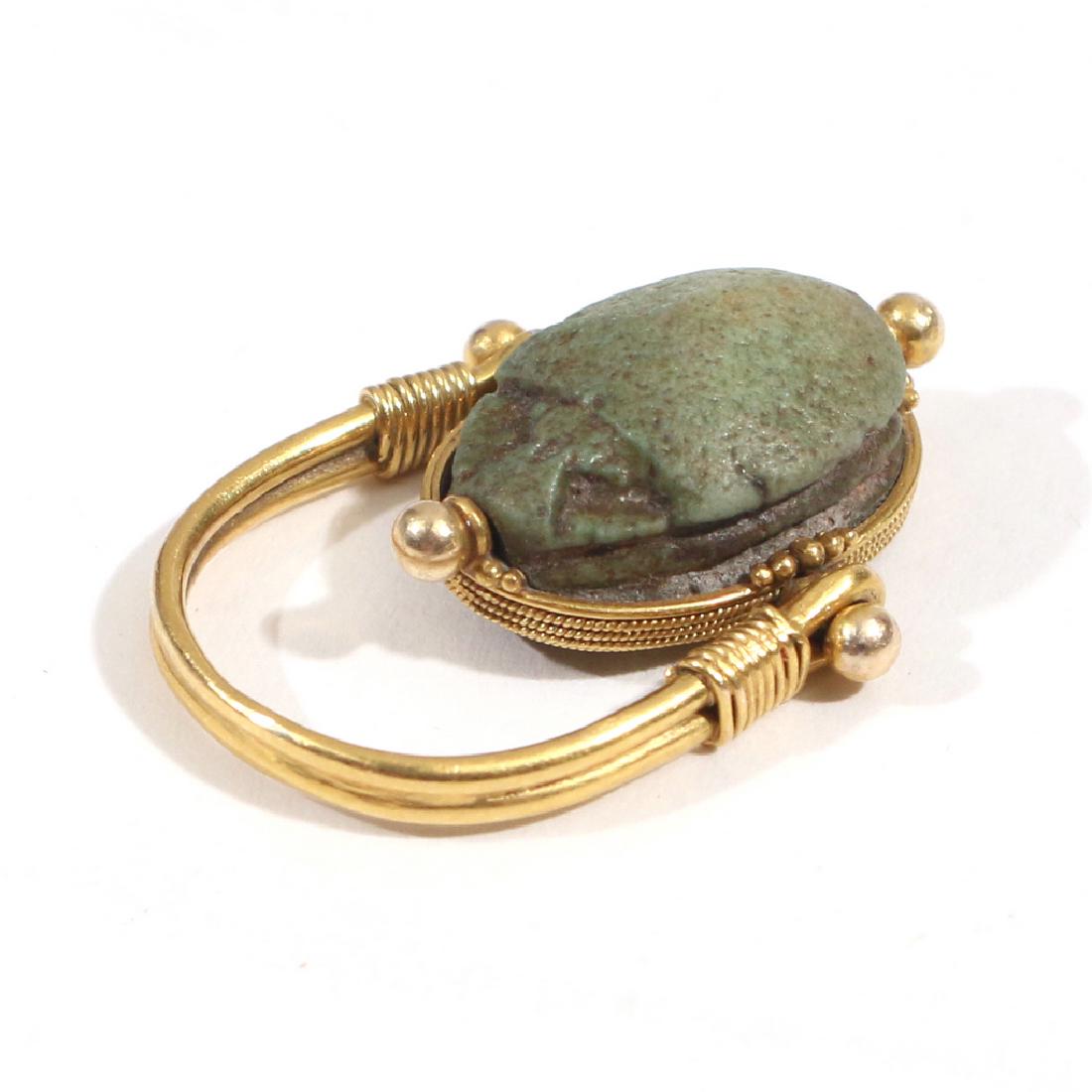 EGYPTIAN FAIENCE SCARAB SWIVEL RING: Having an archaic Egyptian faience scarab (16 x 12 x 7mm) set in a (tested to 14k) gold ropework surround, swivel mounted in a horseshoe shaped ring; 5.3g, size 5-1/2