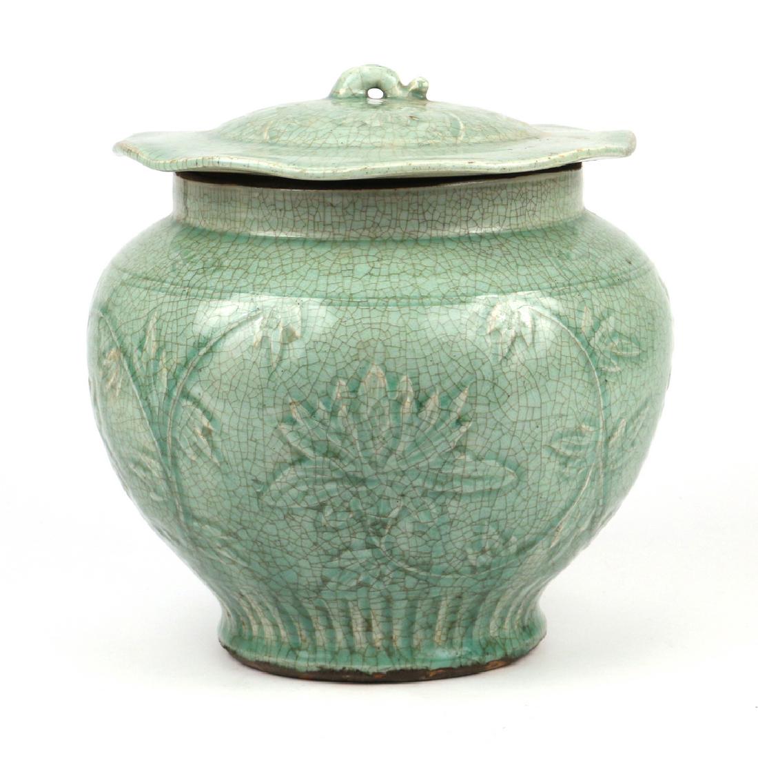LARGE LONGQUAN CELADON COVERED JAR: probably Ming dynasty, the heavy body of bulbous shape with a carved lotus scroll design, the lid with a rippled edge and loop handle, vitrified crackle glaze with small bubbles throughout h. 11-1/2 C