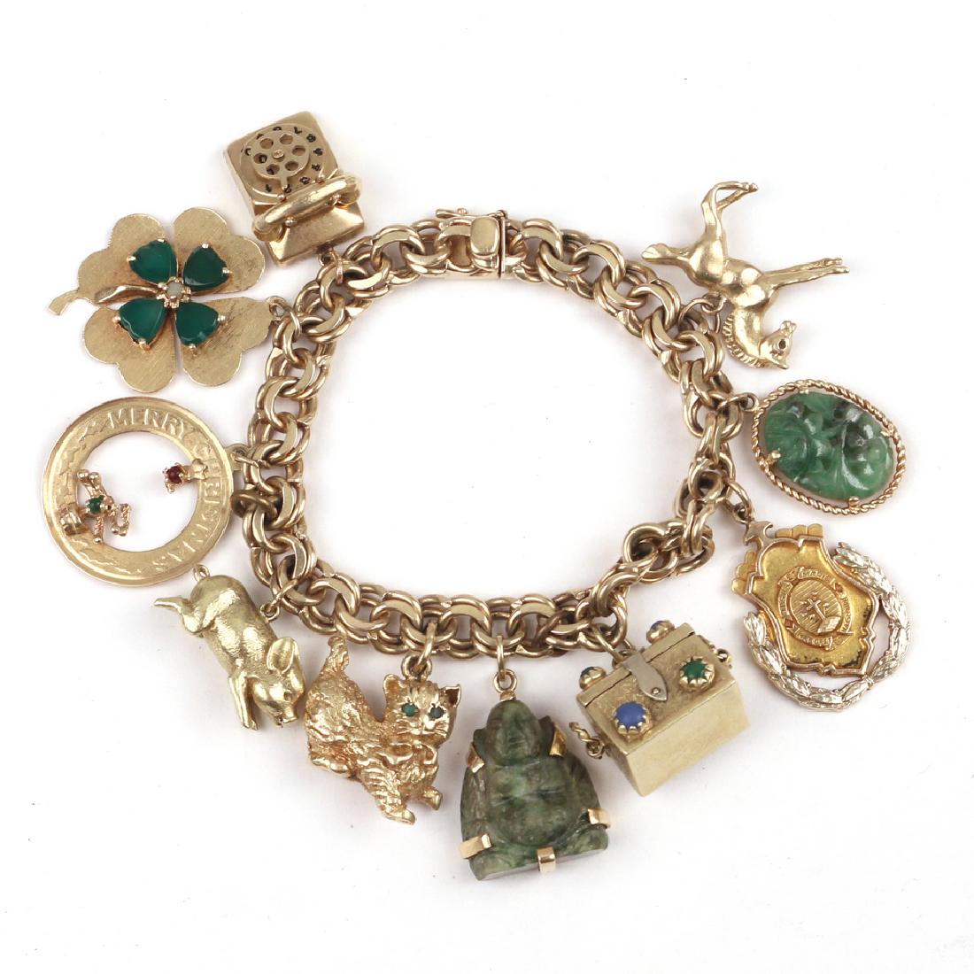 FINE GOLD CHARM BRACELET: Designed as a double-link 14k gold chain suspending 14k gold rotary phone, a 14k four leaf clover, a 14k 'Merry Christmas, an unmarked piglet, a 14k cat with green gemstone eyes, a carved stone Buddha