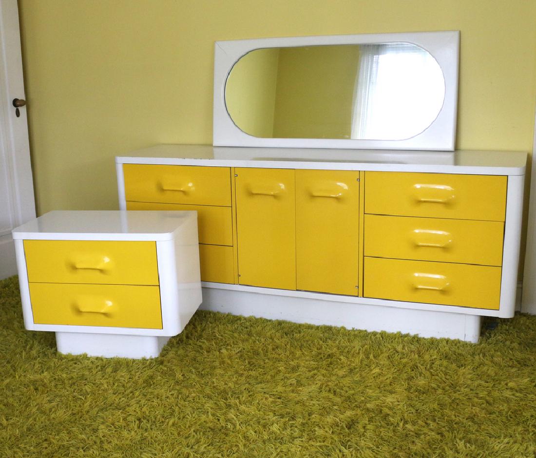 (3pc) BROYHILL PREMIER, RAYMOND LOEWY-STYLE: bedroom suite, including low dresser with yellow plastic molded front and white lacquered cabinet, h. 30 w. 72-1/2 d. 16 in.; night stand, h. 21-1/2 w. 27 d. 16 in., and wall mirror Provenance: Stamfo