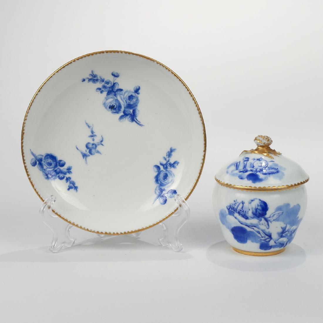 Sèvres PORCELAIN COVERED SUGAR JAR & SAUCER: both painted en camaieu bleu, the sugar jar circa 1765, painted with putti and floral-basket in clouds, with interlacing L mark, M date letter, and artist's mark for Asselin; the saucer circa 1771, pa