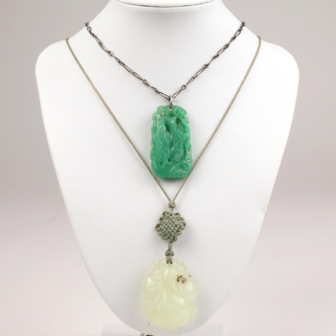 (2pc) CARVED JADE PENDANTS: Including a green jade carved reticulated pendant showing a man next to a tree (1-7/8 x 1 in.) on a silver chain (27.9g with chain), and a pale green jade pendant carved with blossoms and leaves, incl