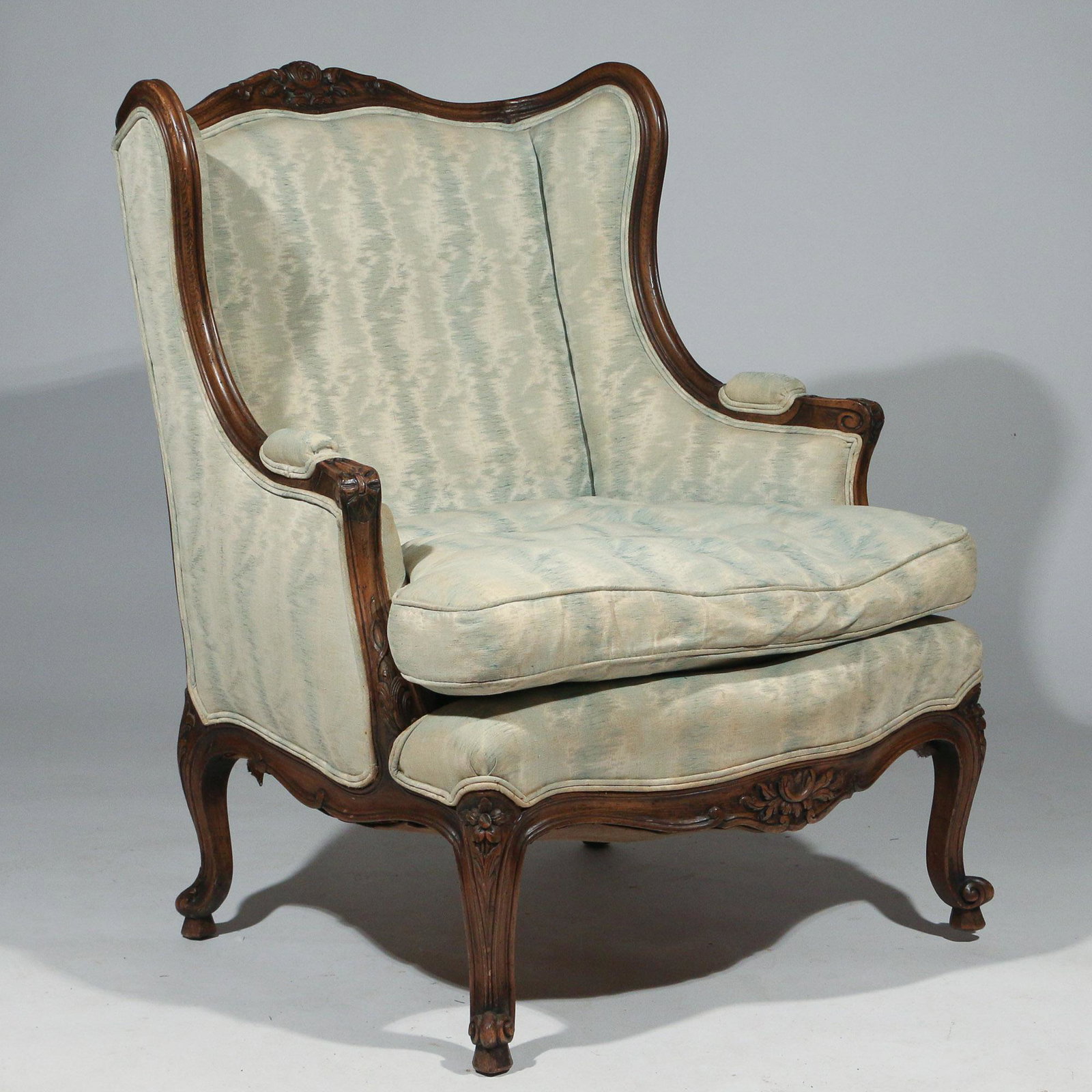LOUIS XV STYLE BERGERE A OREILLES CHAIR: 18th century or later; crested by floral spray, upholstered armrests with outset carved handholds, cabriole legs; with down cushion h. 38 w. 30 d. 33 in.